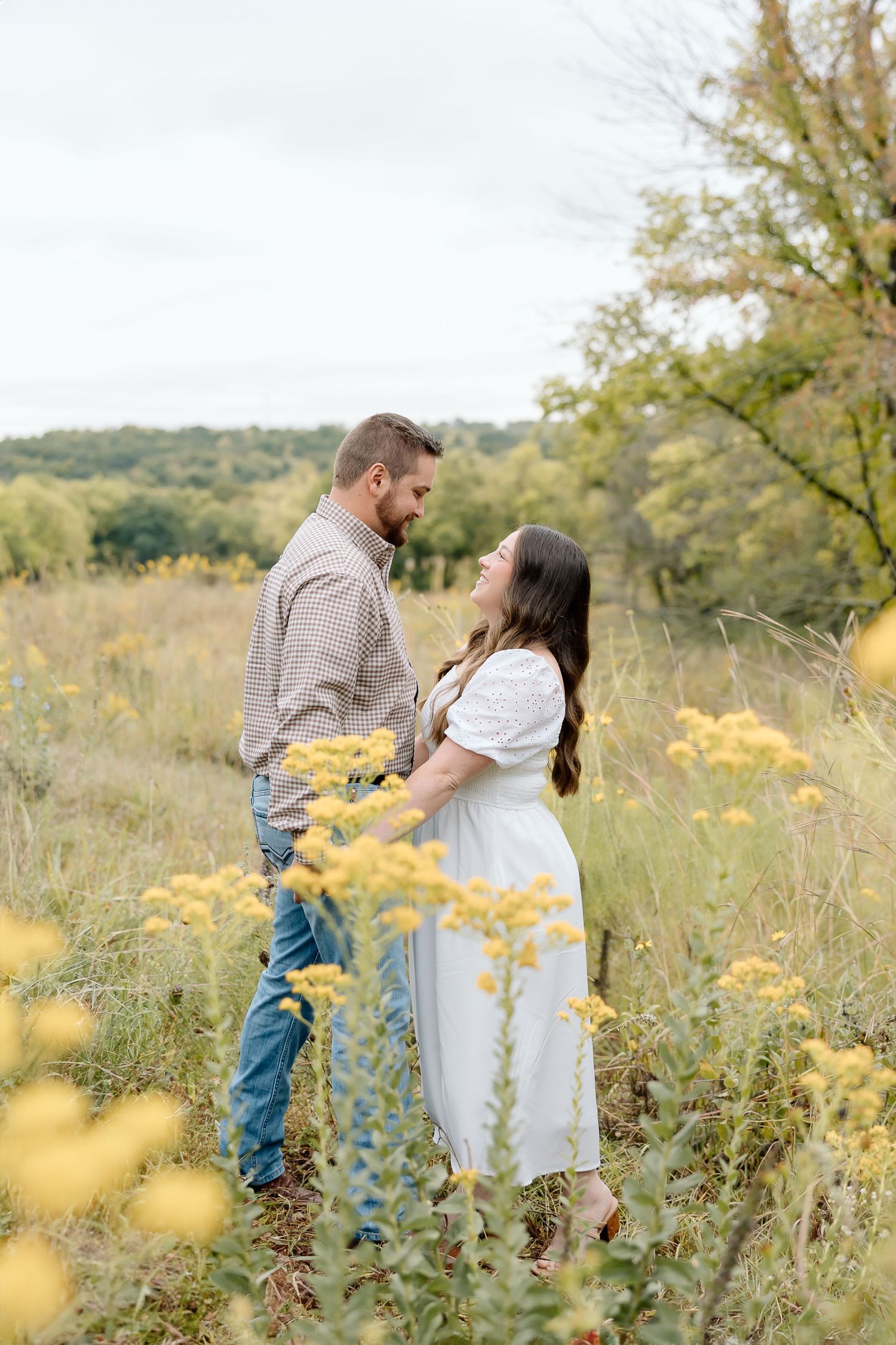 Romantic portrait of couple standing together in wildflower meadow with rolling landscape behind.