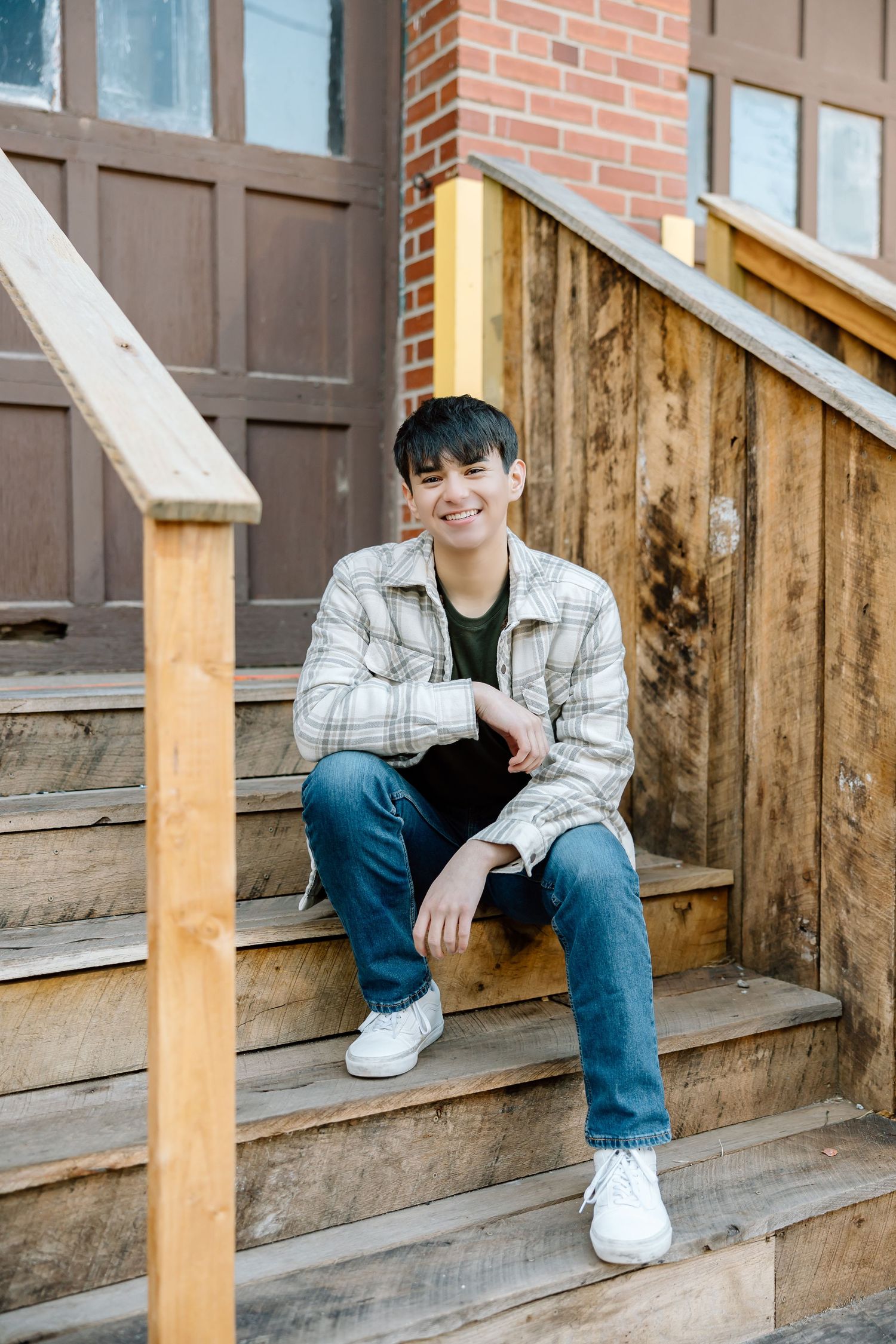 Person in casual wear smiling while sitting on wooden stairs with rustic door background.