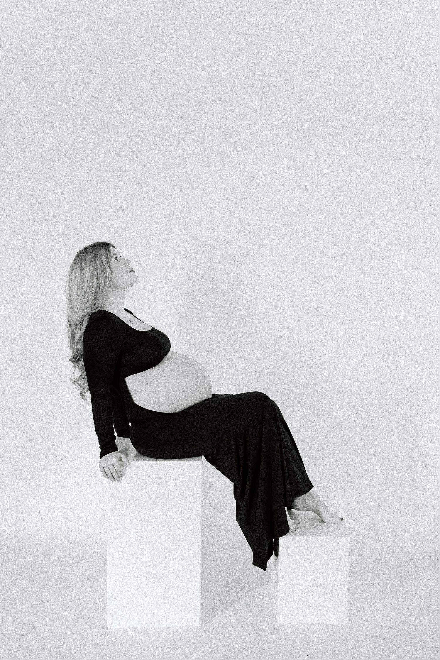 Black and white photo of pregnant woman sitting gracefully on geometric white blocks.