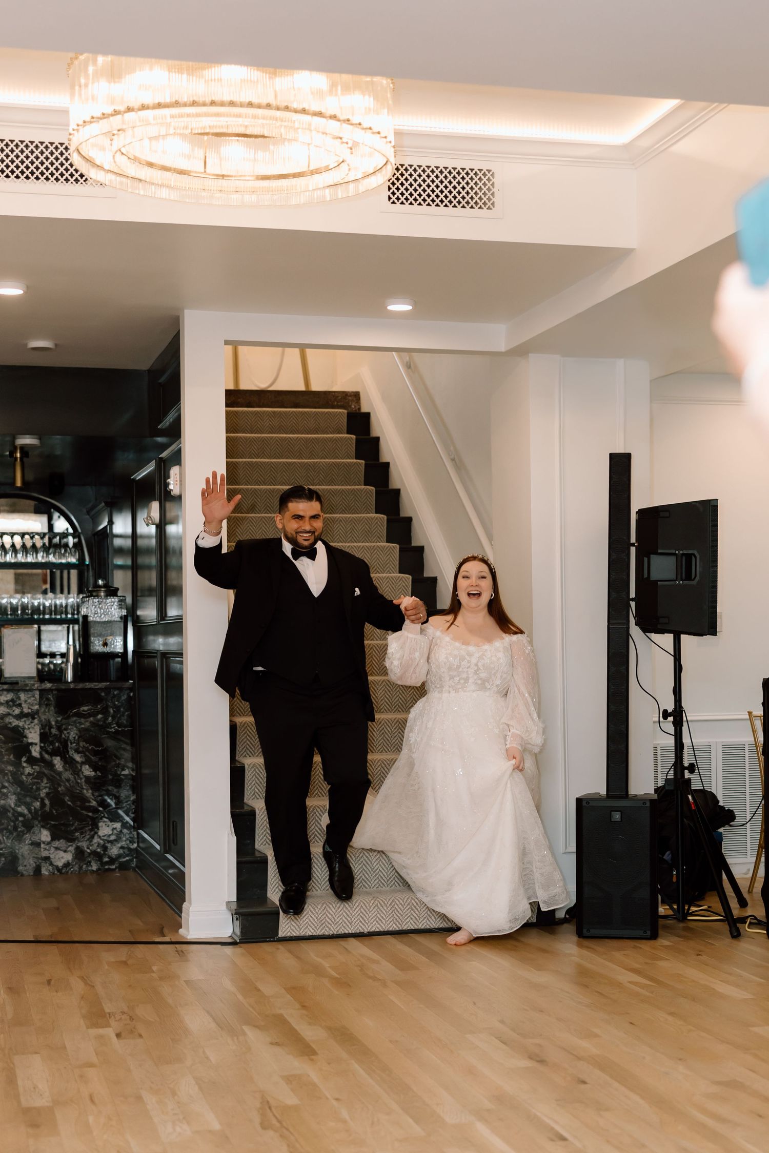 Bride and groom make grand entrance descending staircase at elegant wedding reception venue.