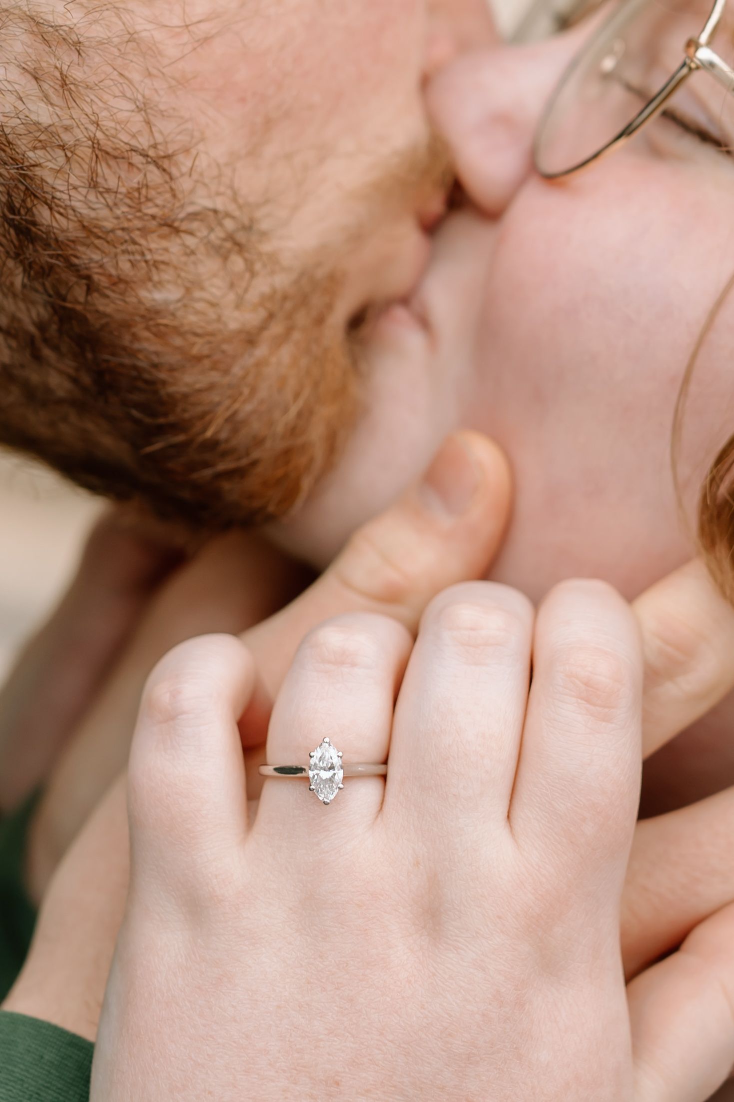 A romantic kiss between two people with a diamond engagement ring prominently displayed on the hand.