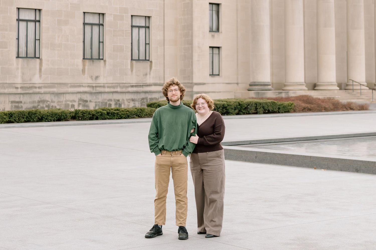 Couple sits on stone steps of a grand neoclassical building in a romantic pose.