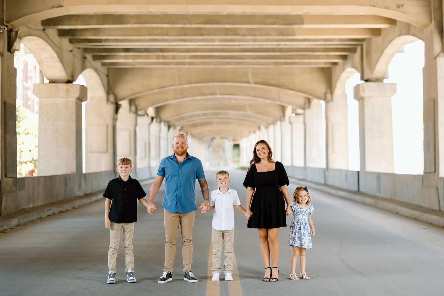 A family stands together under a covered walkway with stone columns and archways.