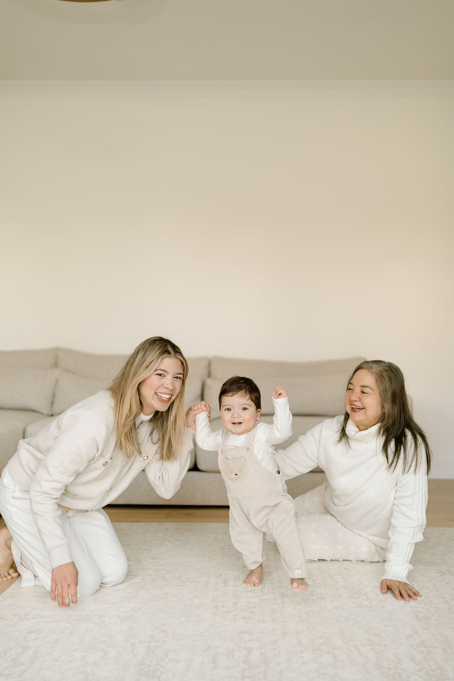 Three people in matching white outfits crawl and play together on a light colored carpet.