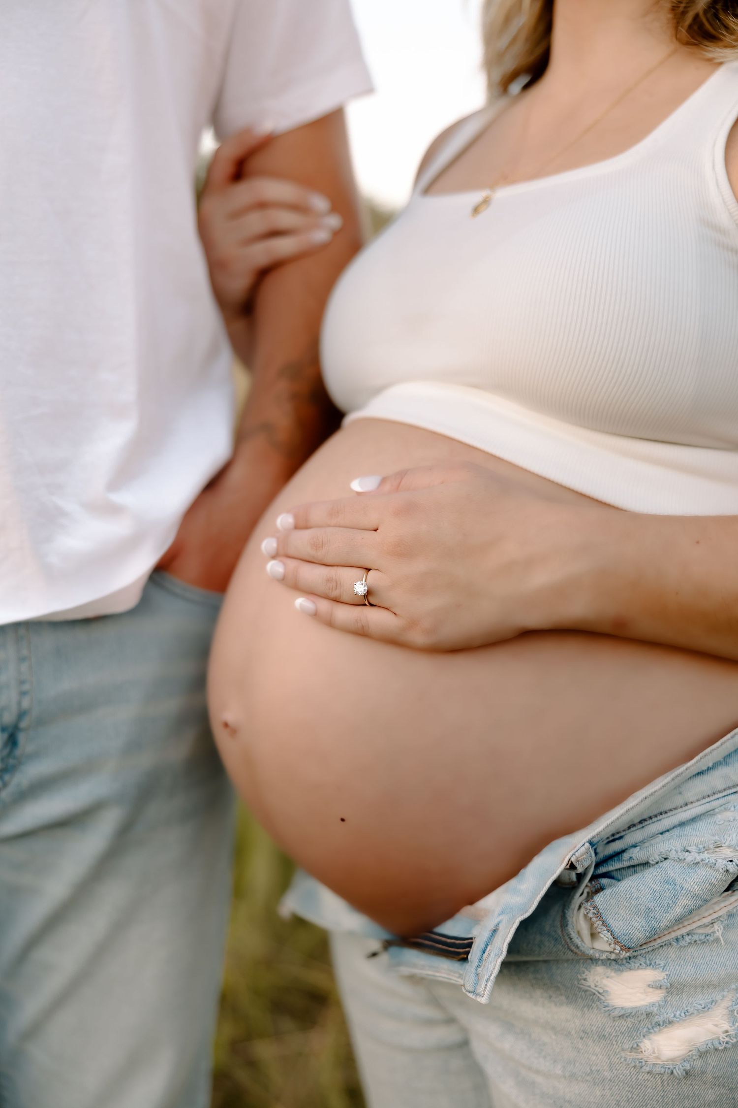 A series of photos showing a growing baby bump in distressed denim jeans and white top during pregnancy progression.
