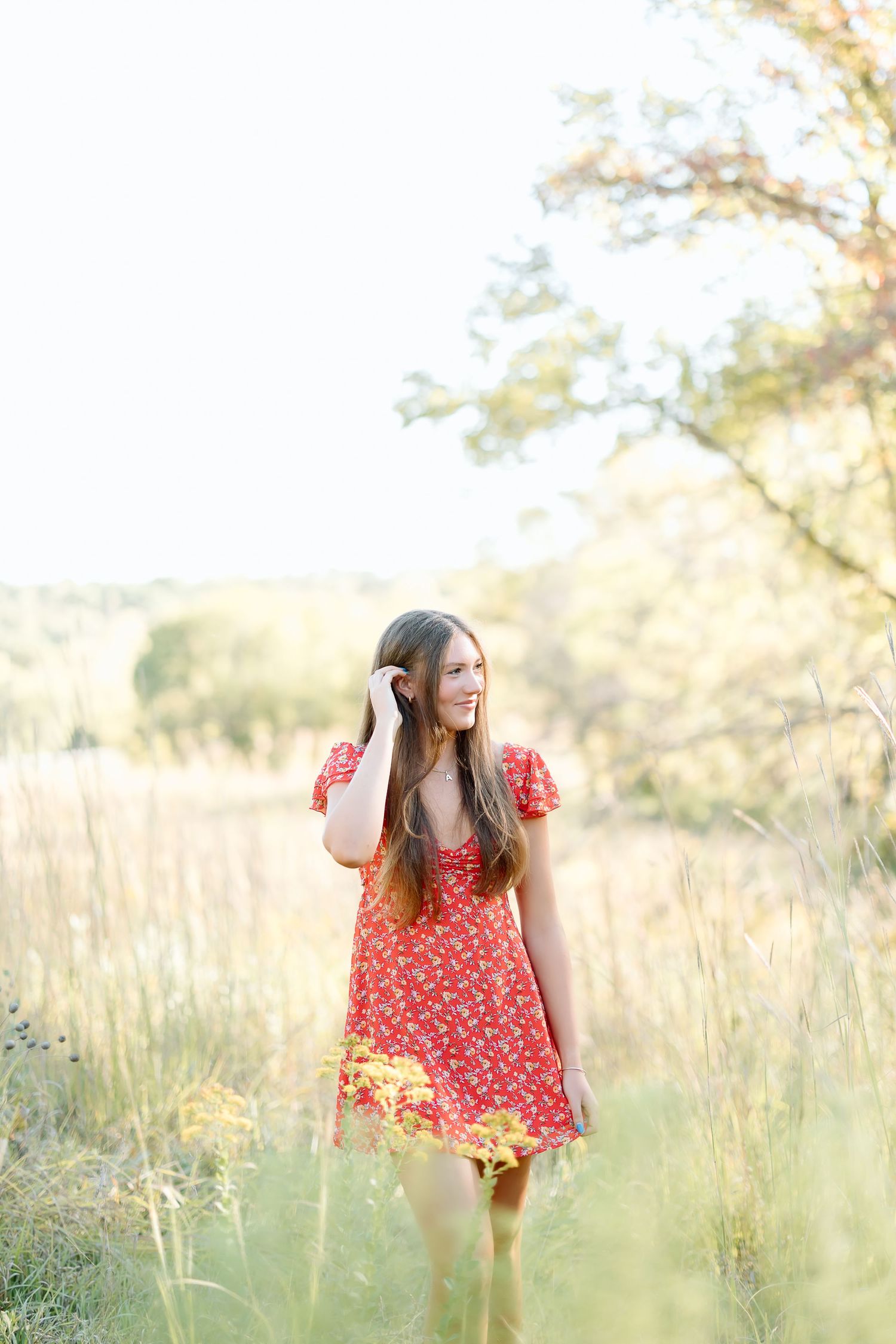 A person in a red floral dress walks through a sun-drenched meadow of tall grass during golden hour.