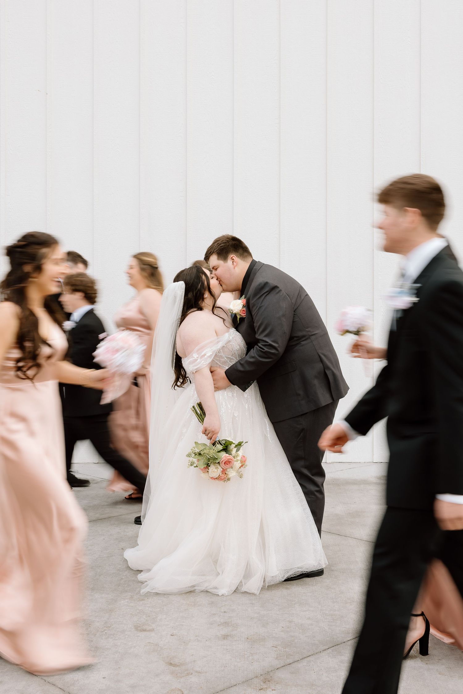 Motion blur captures elegant dancers in formal attire twirling across a bright white dance floor at a wedding reception.