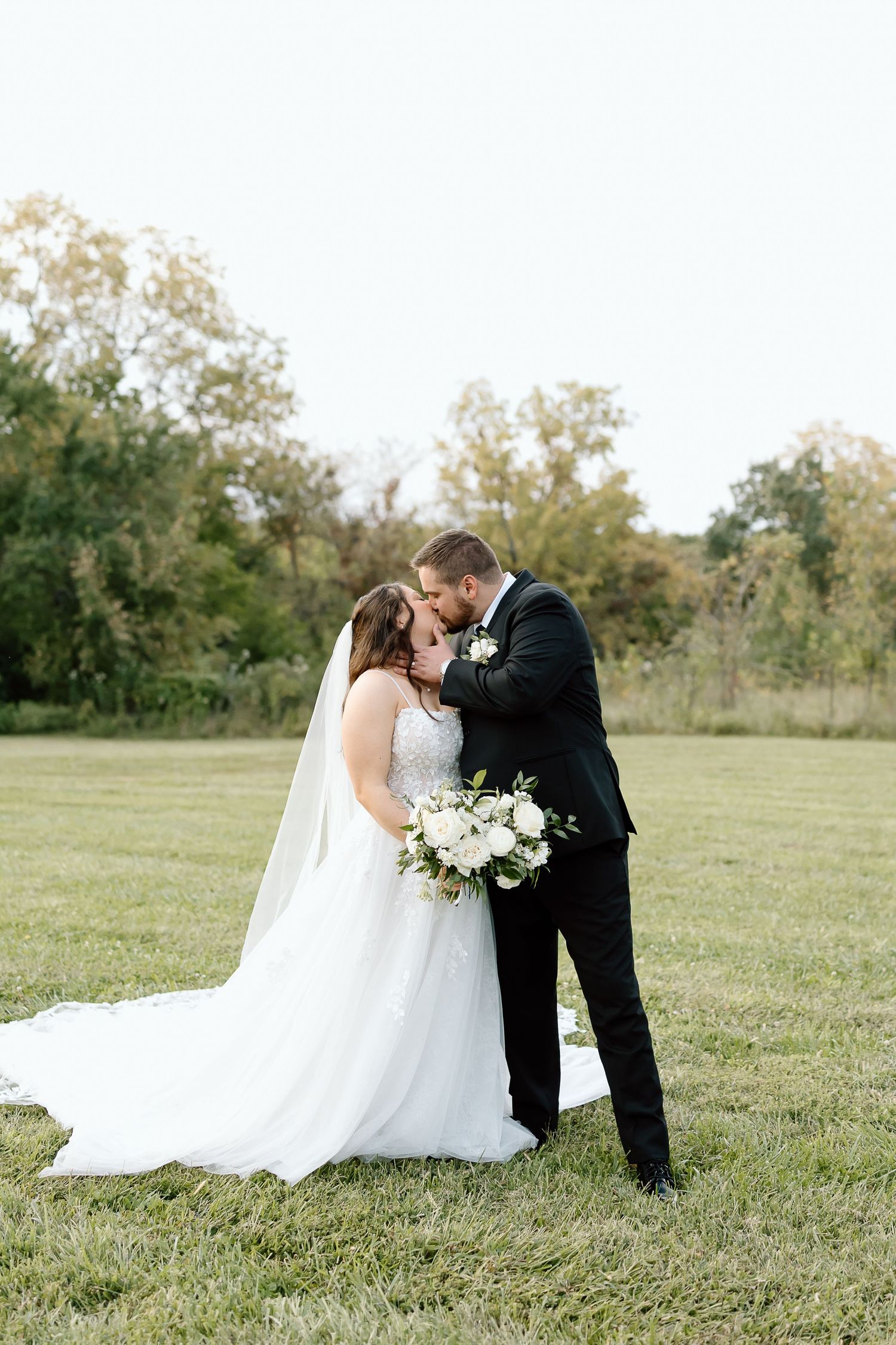 A romantic wedding couple shares an intimate moment in a serene outdoor field setting.