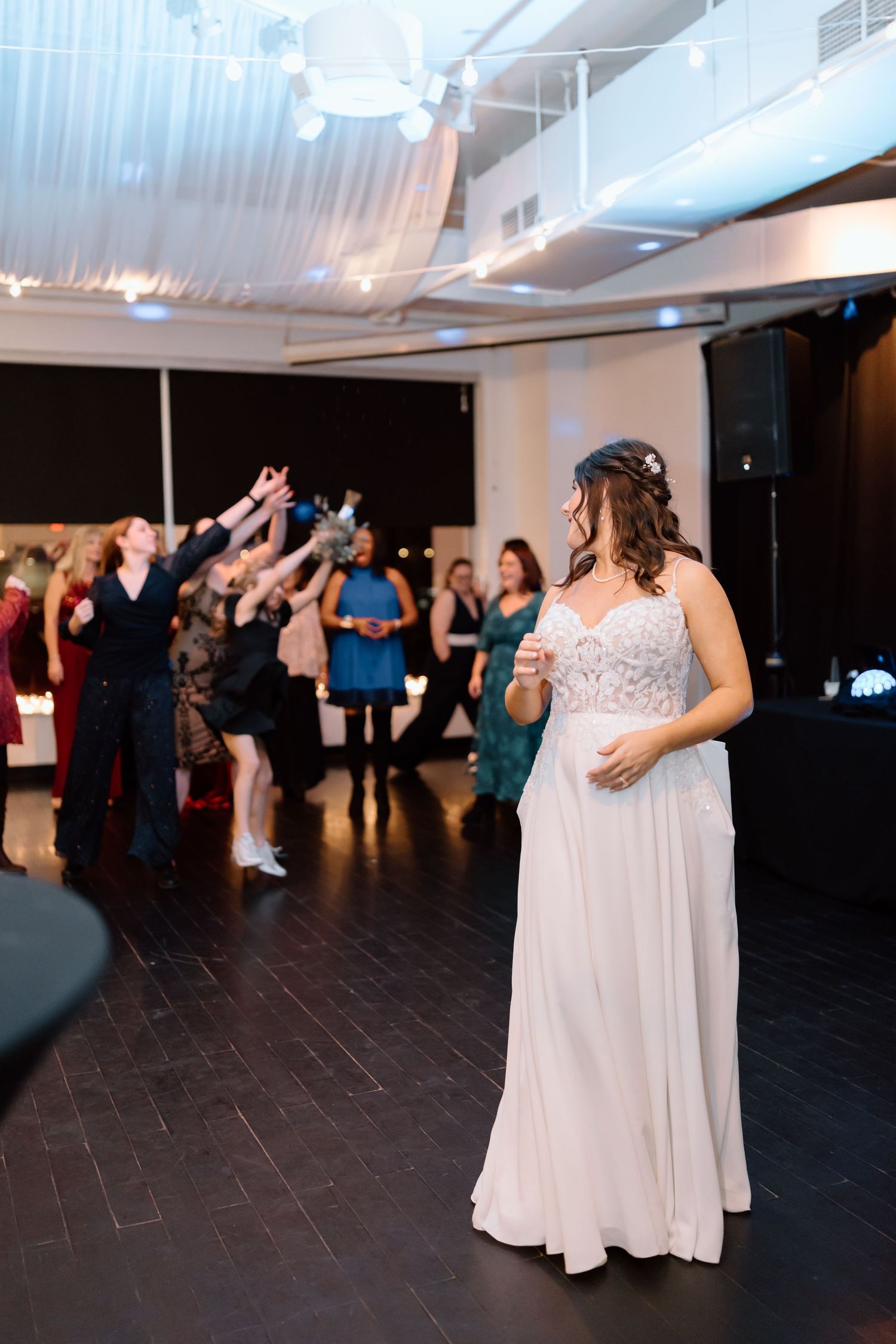Wedding guests dance and celebrate on a dark dance floor at an indoor reception venue.