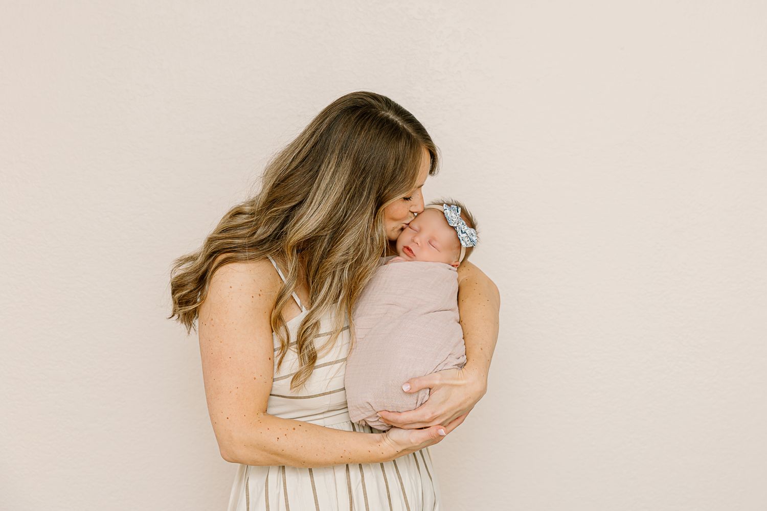 Intimate moment between parent and sleeping newborn against beige background.