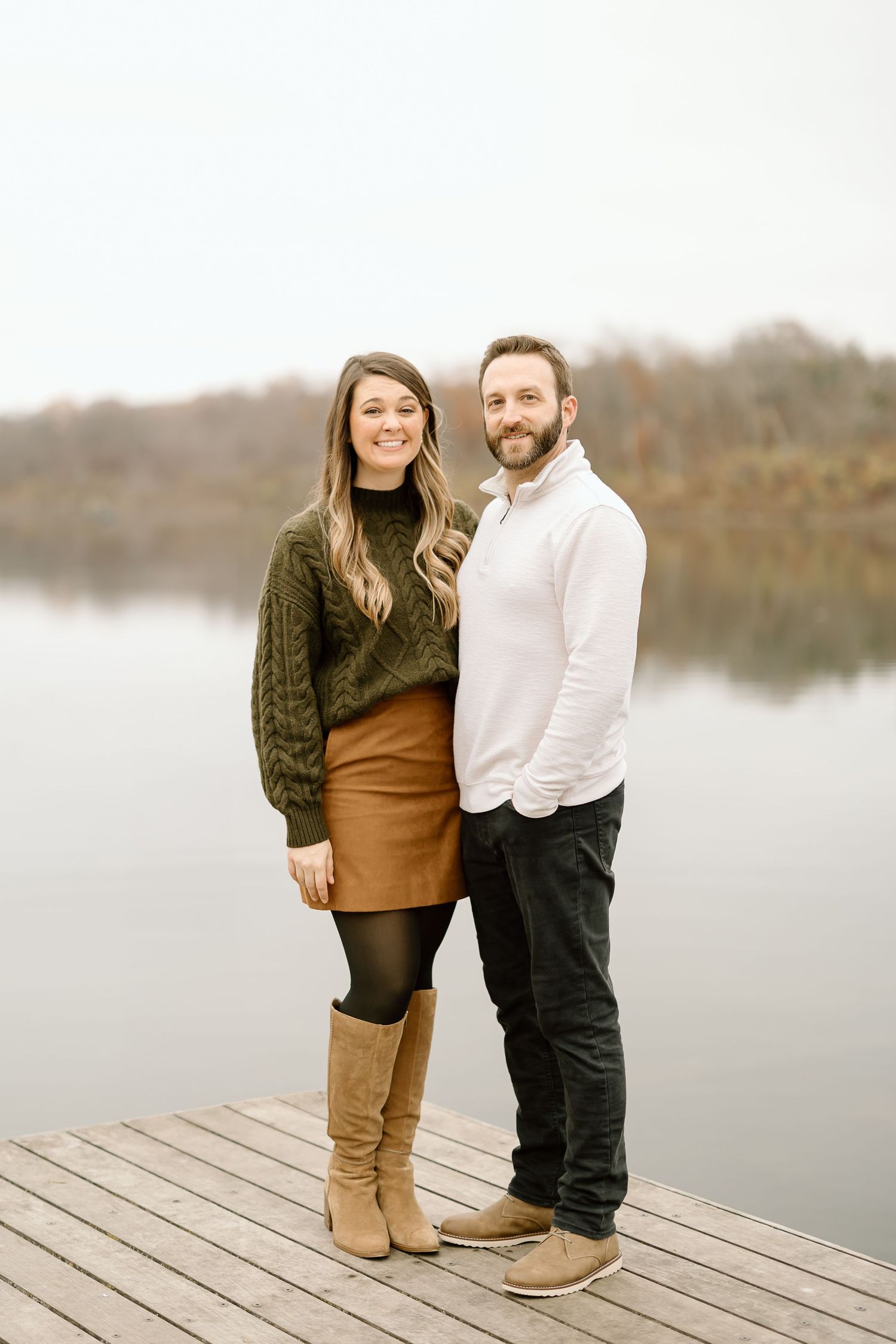 Couple in coordinated casual wear poses together on wooden dock by tranquil lake.