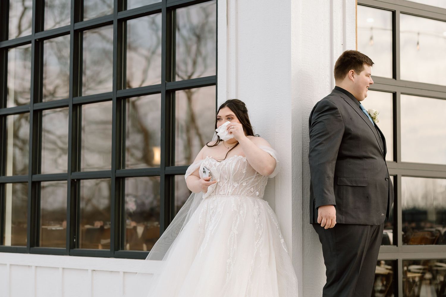 Bride and groom standing apart during first look photos against modern building.