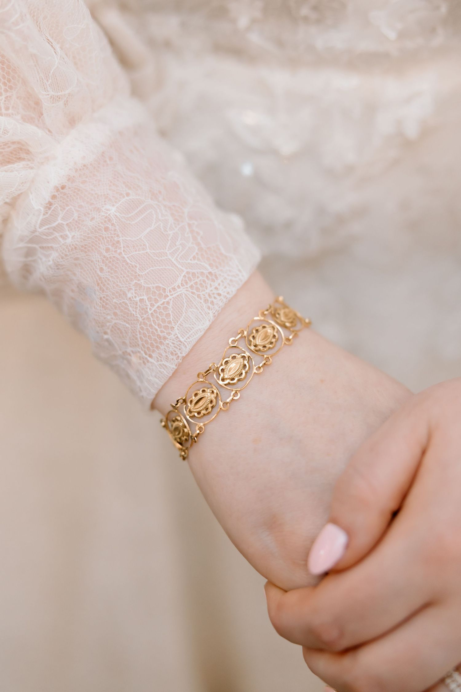 Close-up of a gold filigree bracelet on a bride's wrist wearing a white lace wedding dress sleeve.