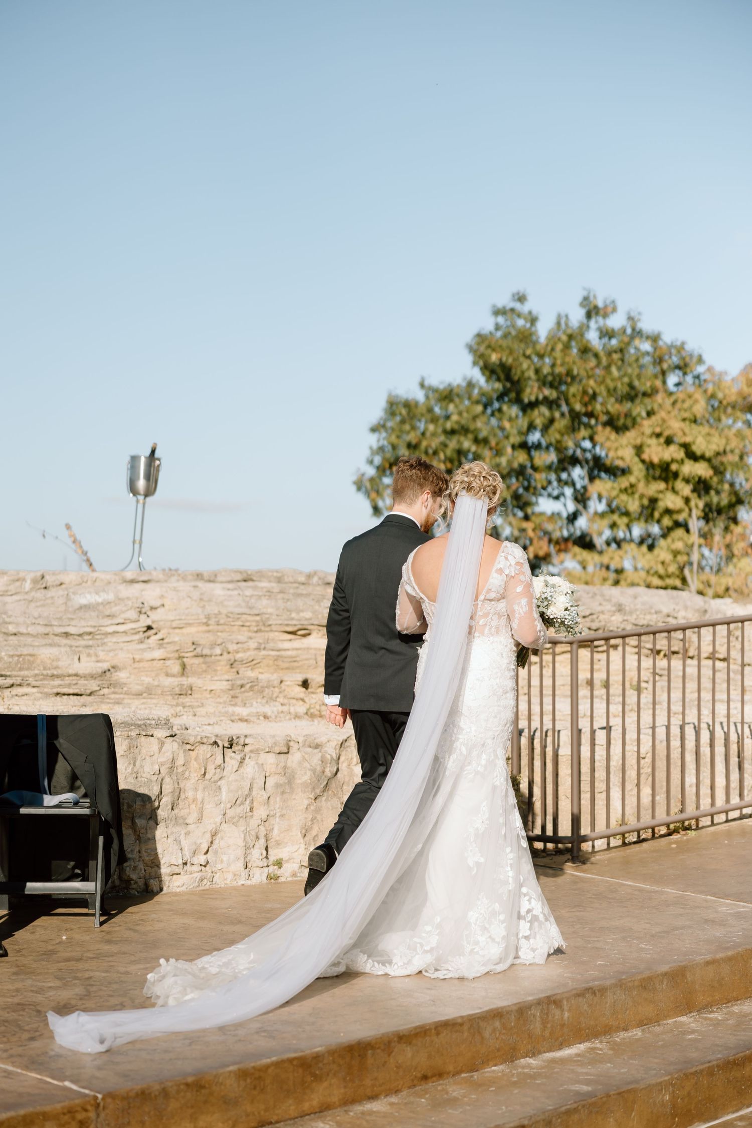 A bride and groom sit together at a piano on a stone terrace during their wedding photoshoot.