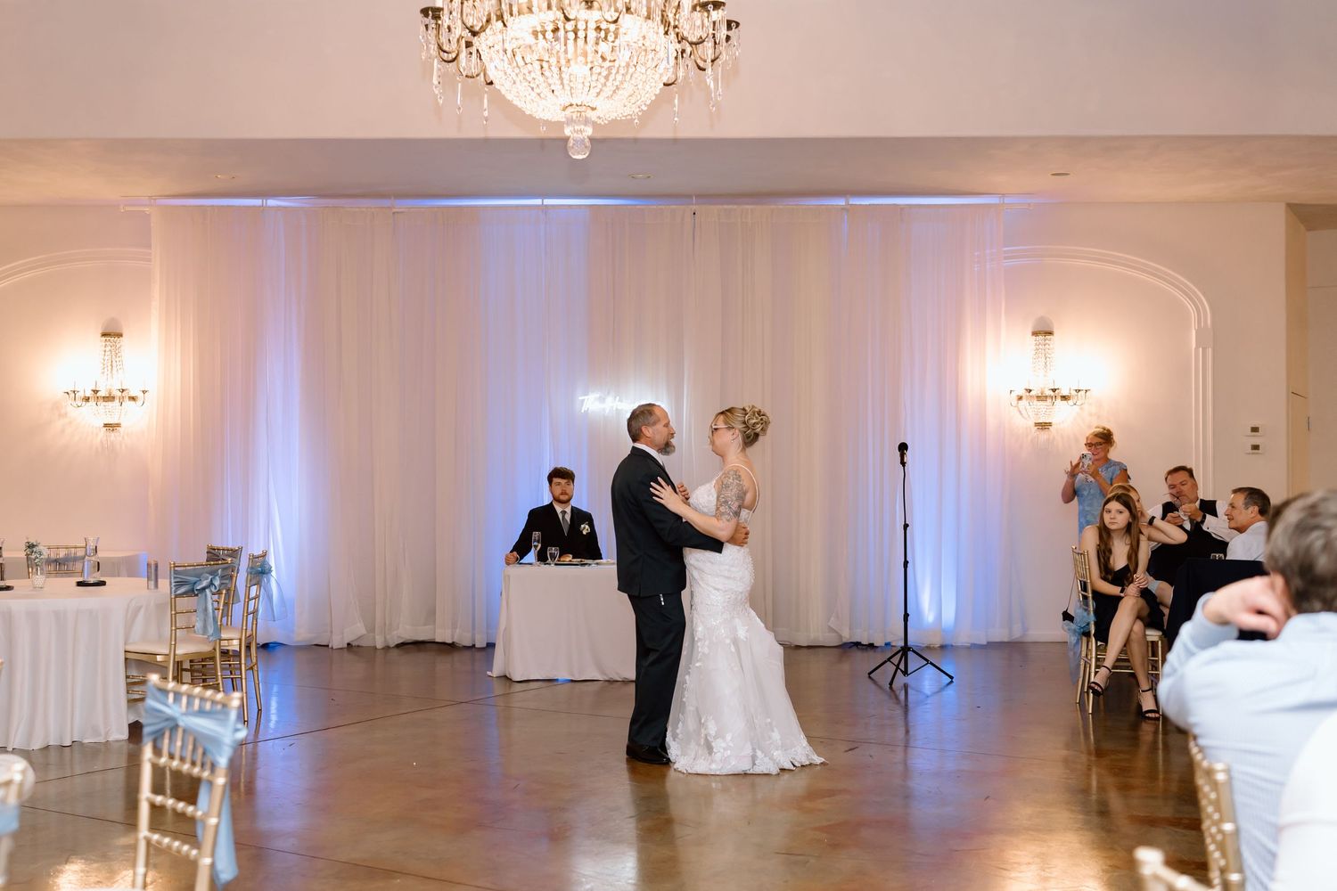 Elegant white ballroom with crystal chandeliers and white drapery creates a romantic atmosphere for a wedding reception.