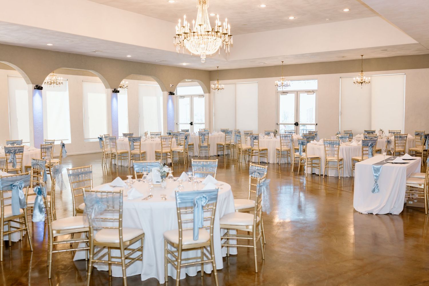 Elegant white ballroom with crystal chandeliers, gold chiavari chairs, and floor-to-ceiling windows for wedding receptions.
