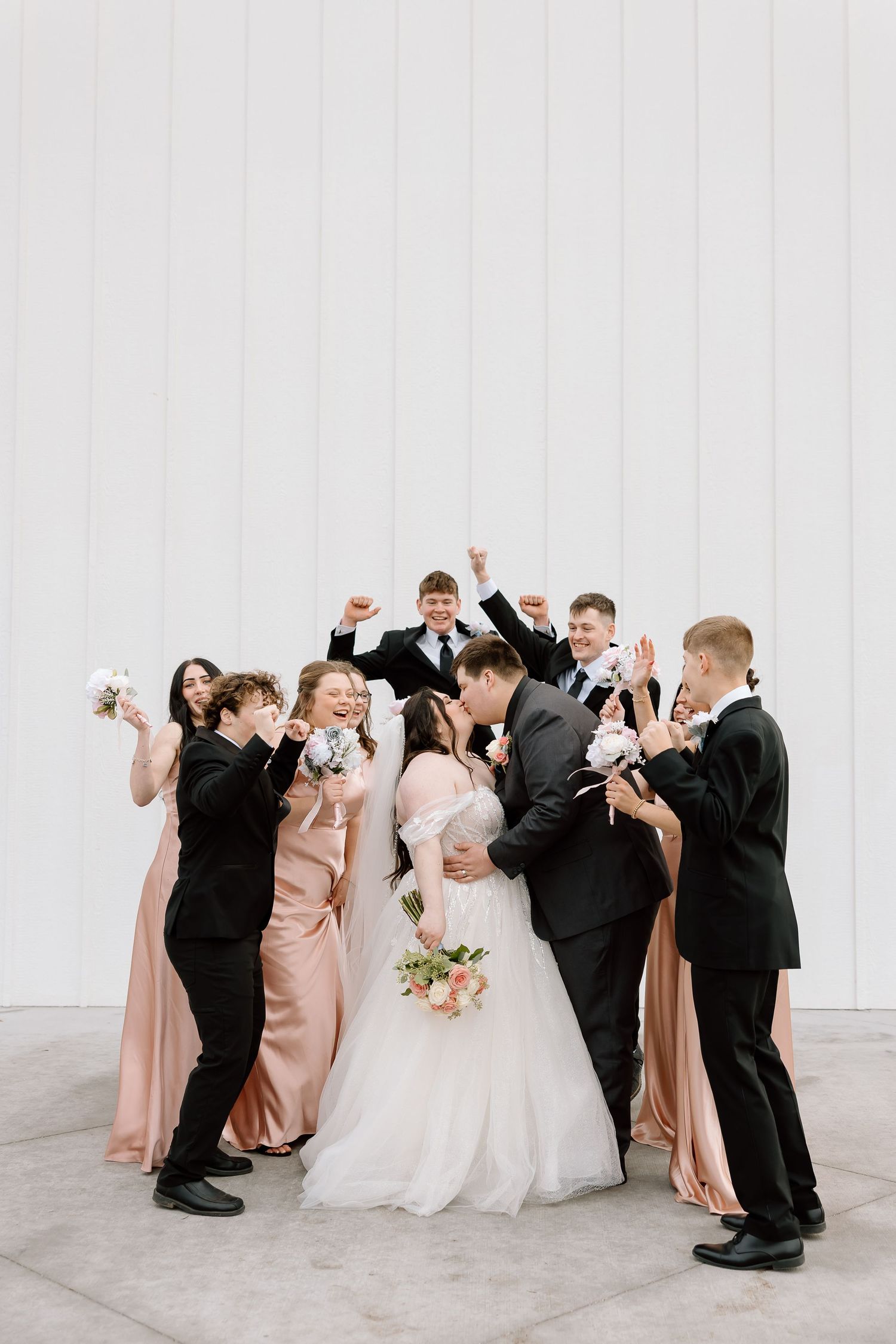 Wedding party in blush pink dresses and black suits poses playfully in sequence of celebratory dance moves.