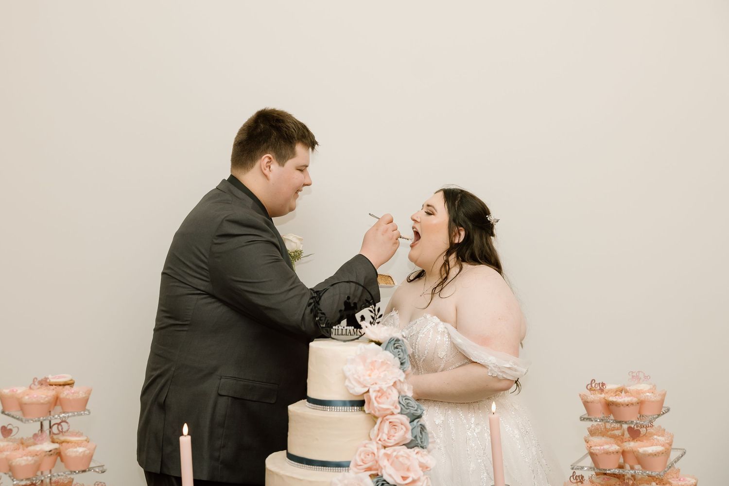 A couple shares a romantic moment while cutting their pink wedding cake at an elegant reception.