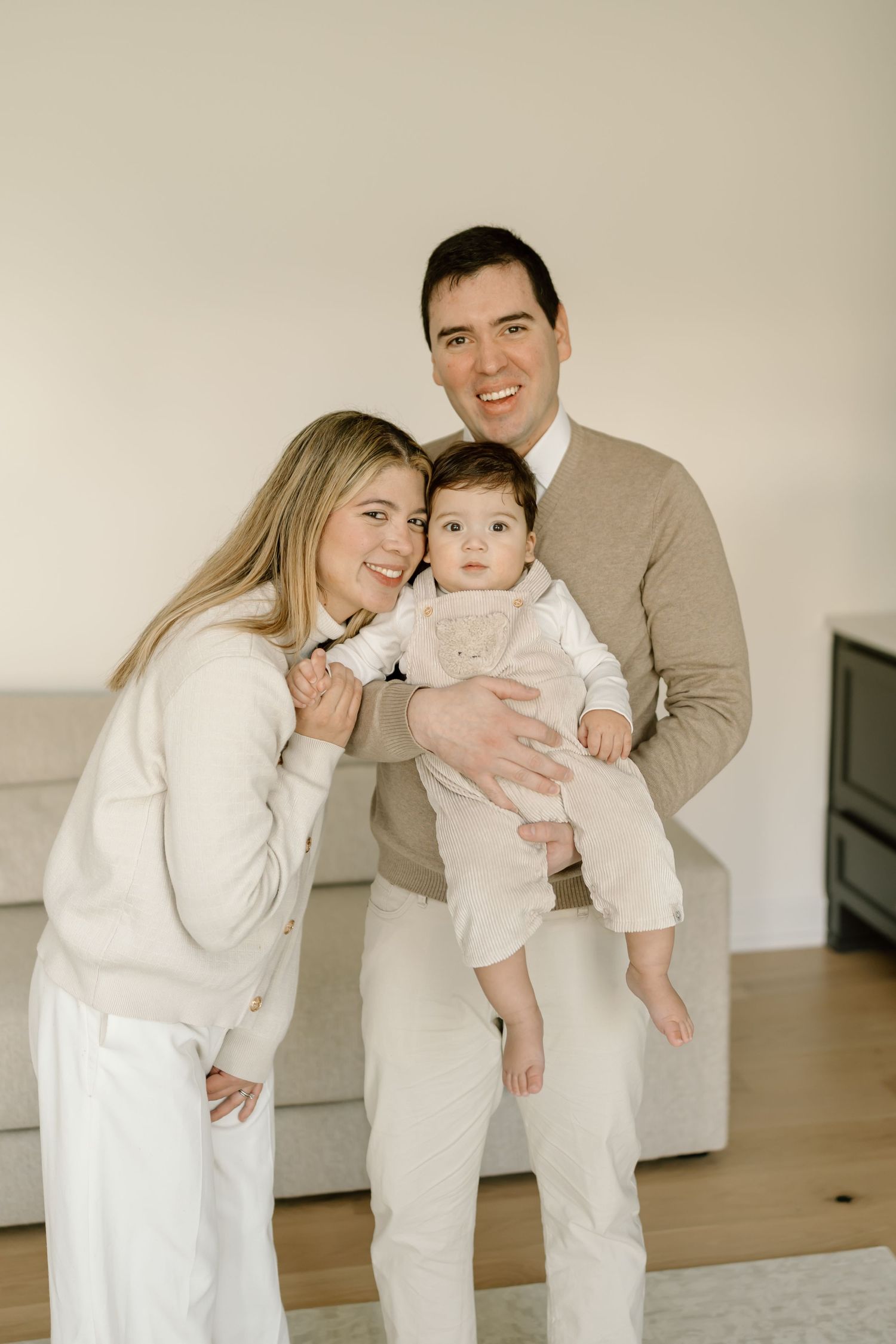 Family wearing coordinated white and beige outfits poses together in a series of candid shots at home.