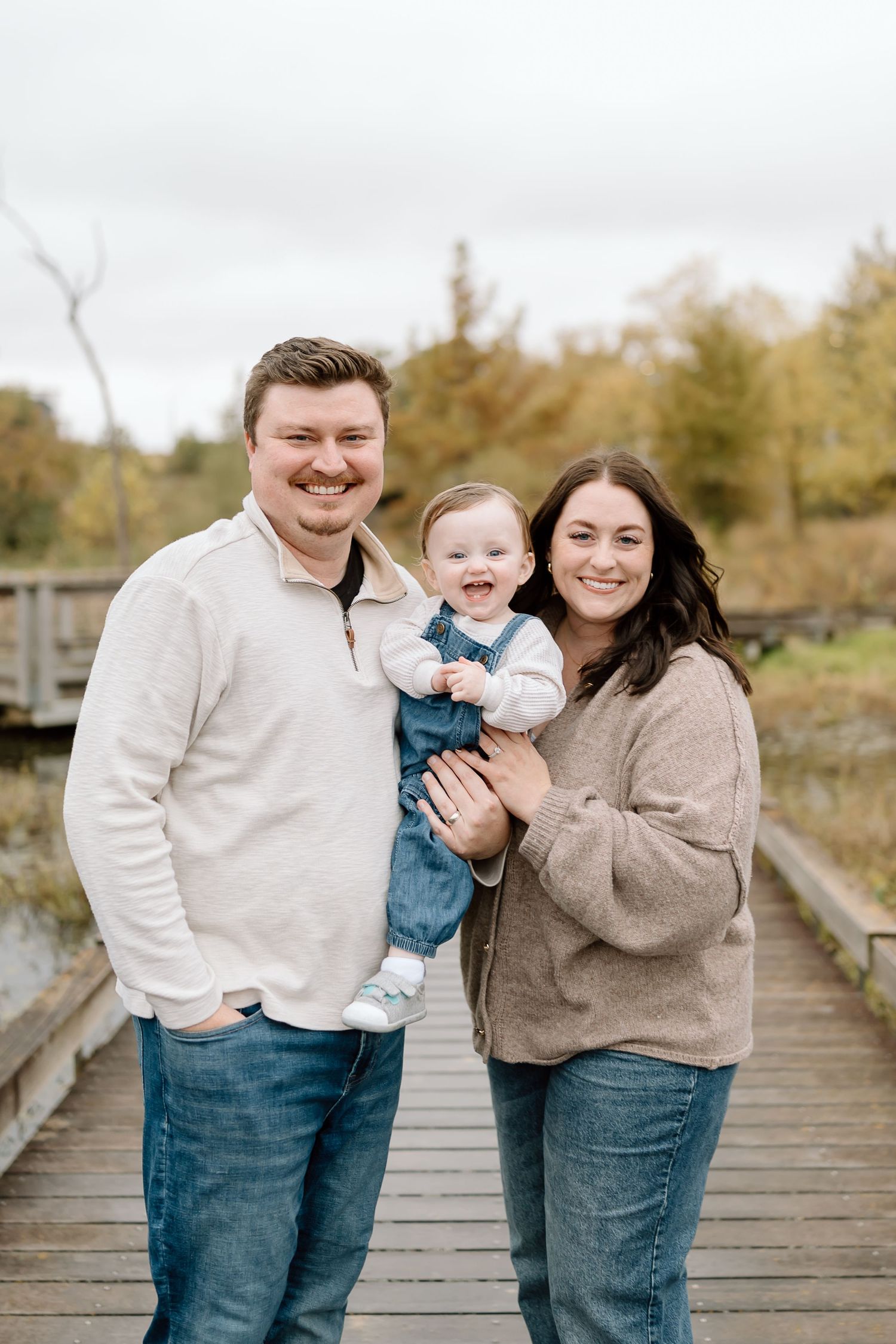 A family shares joyful moments together on a wooden boardwalk during an autumn photoshoot.