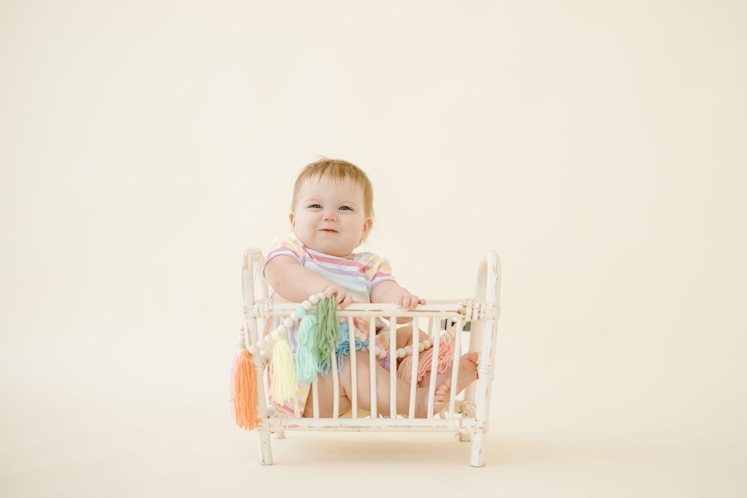A baby in a white crib with pastel decorative elements against a light neutral background.