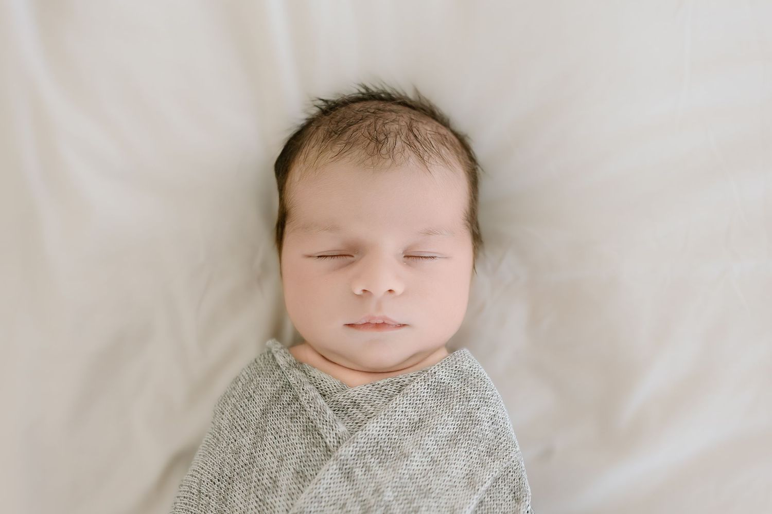 A sleeping baby lies on white bedding in a series of peaceful poses.