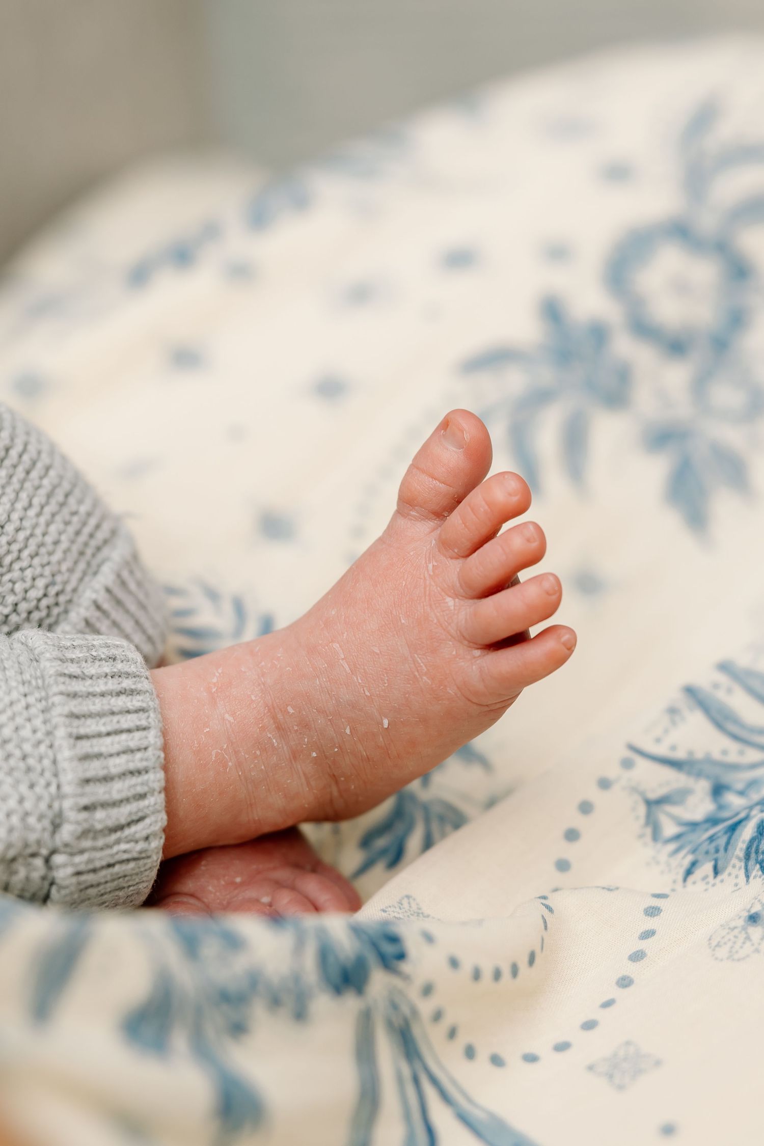 A tiny baby's foot rests on a white blanket with delicate blue floral patterns.