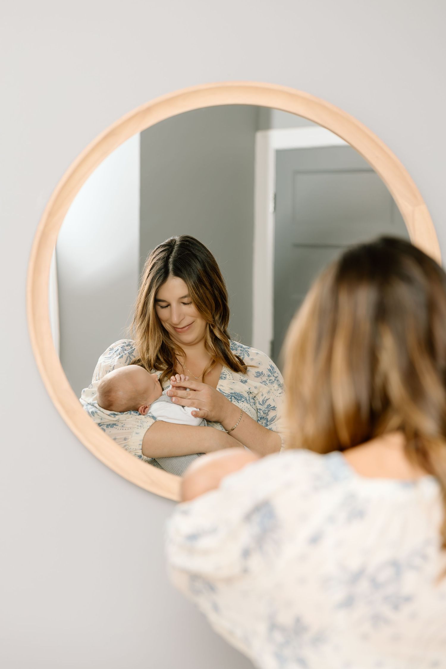 A series of mirror reflections show someone in a floral print dress looking down while standing at a vanity.