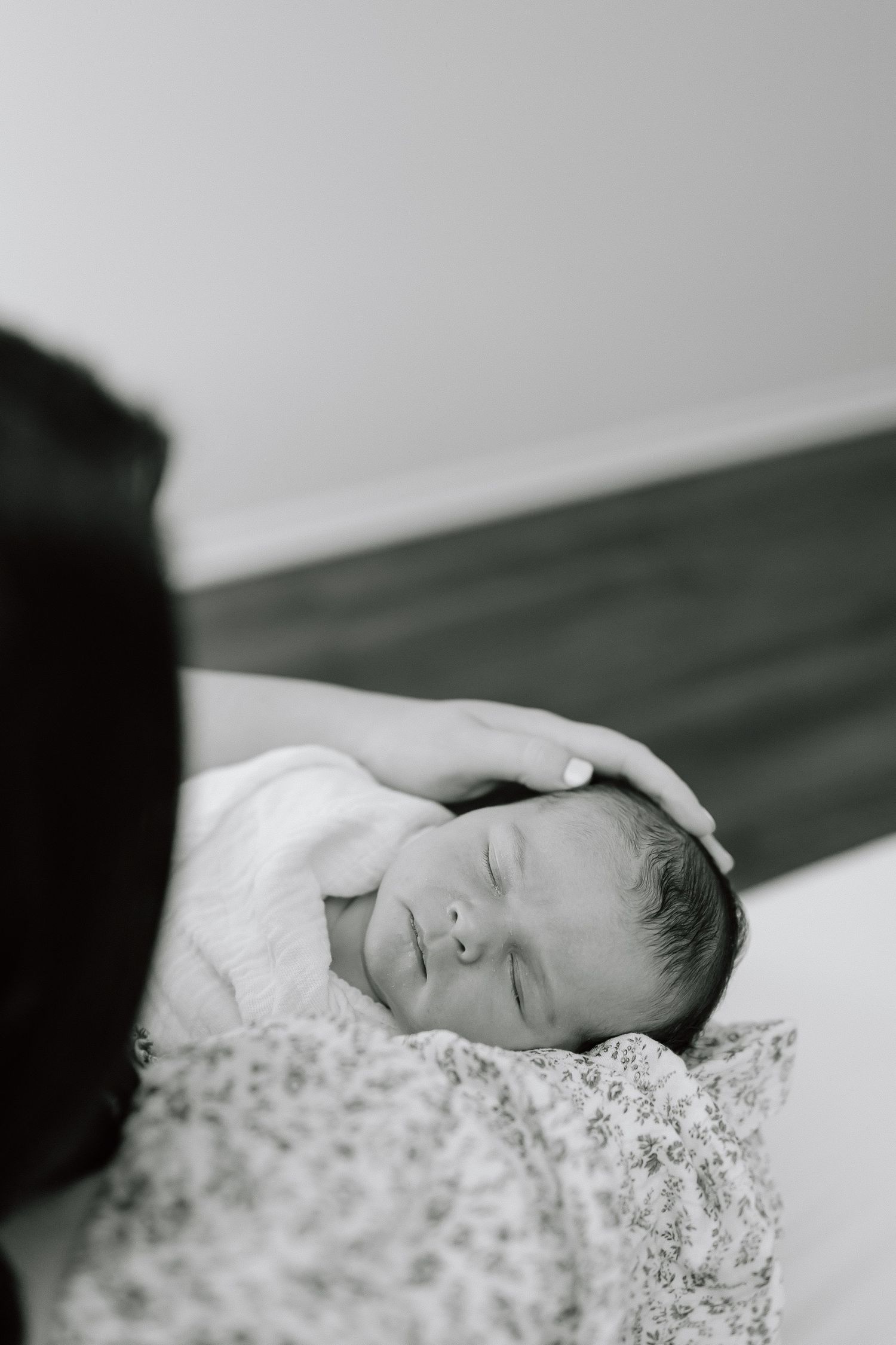 A tender black and white photograph of a sleeping newborn baby resting on floral patterned fabric.