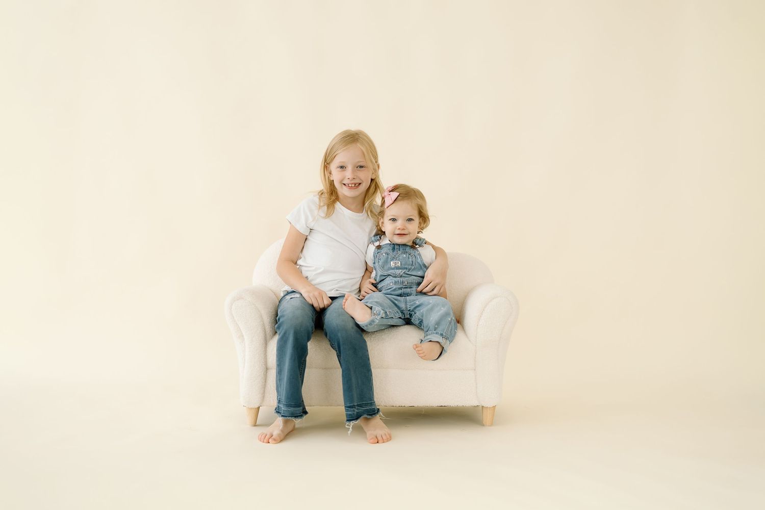 Siblings in matching denim sit and play together on a white backdrop in a casual photo session.