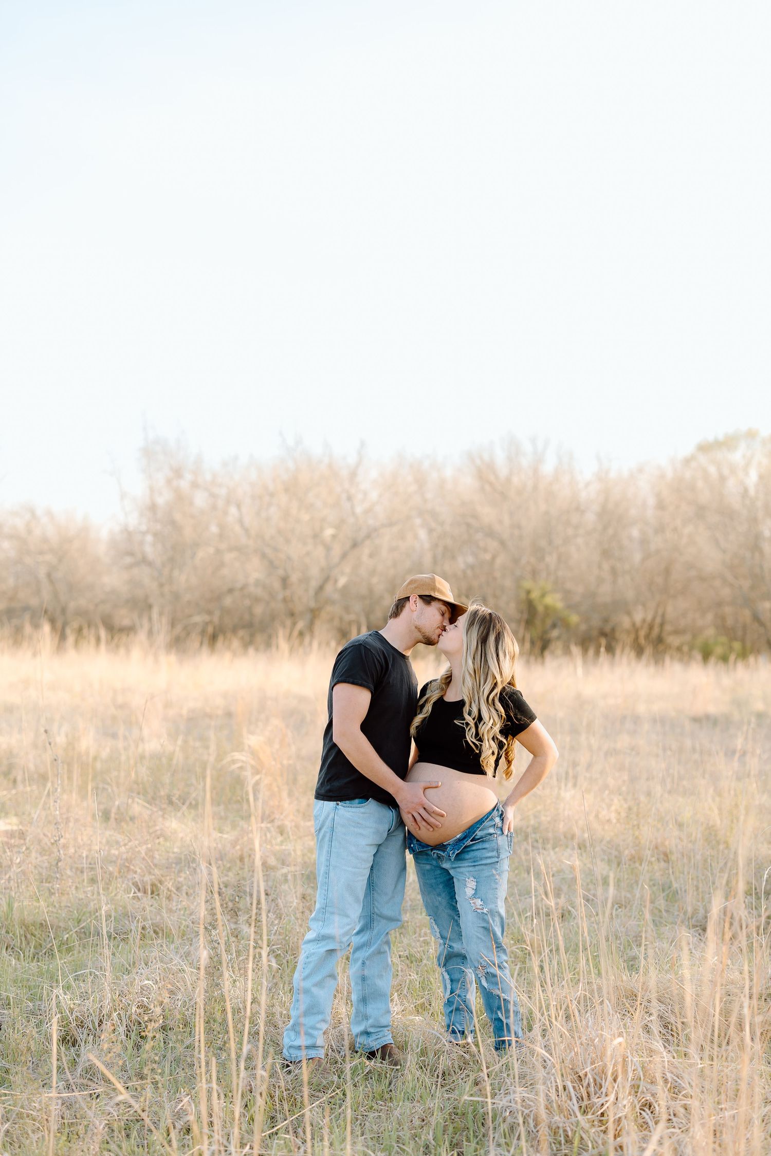 A romantic couple embraces in a golden field of tall grass during sunset.