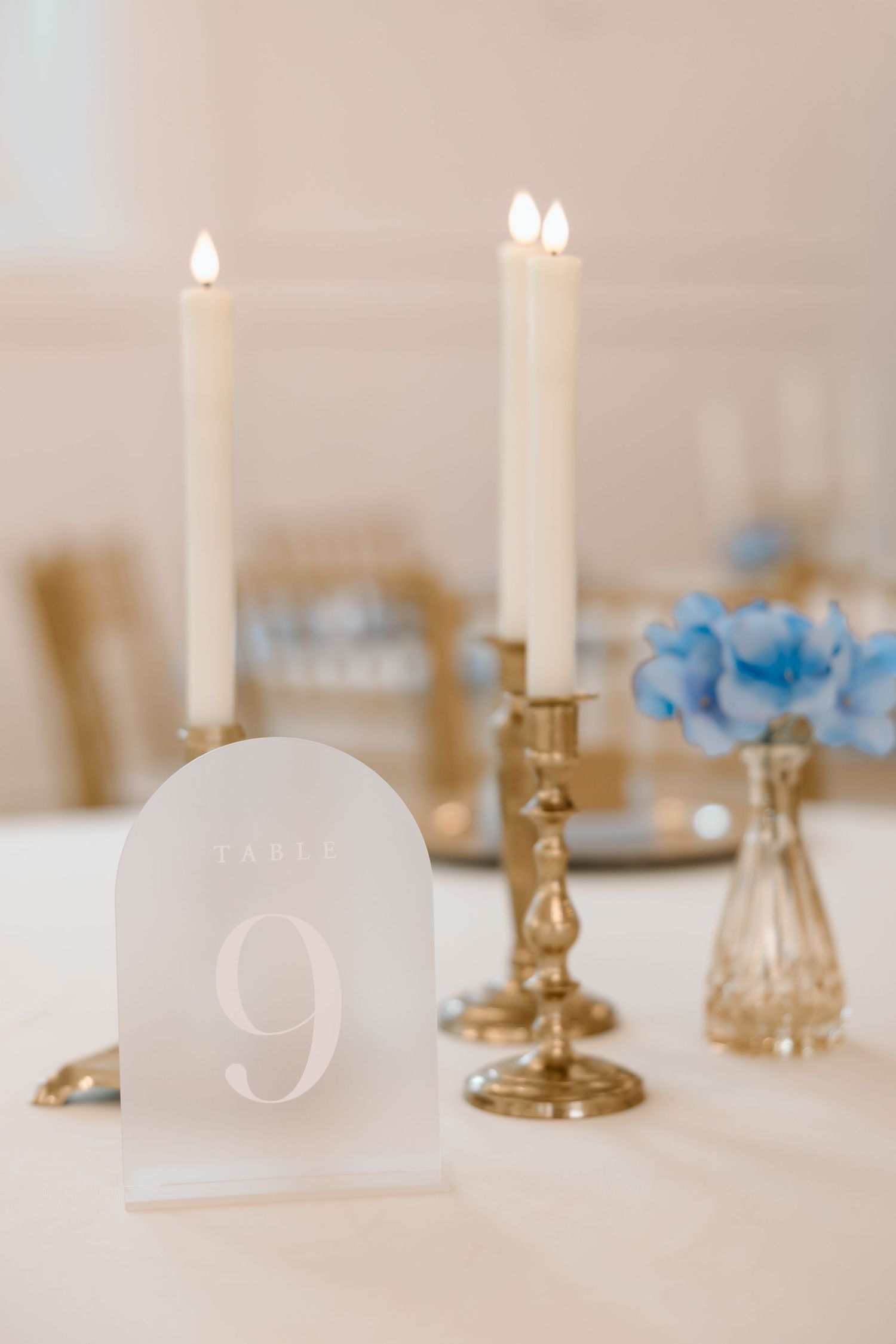Elegant wedding table setting with arched Table 9 sign, gold candlesticks, lit taper candles, and blue hydrangeas.