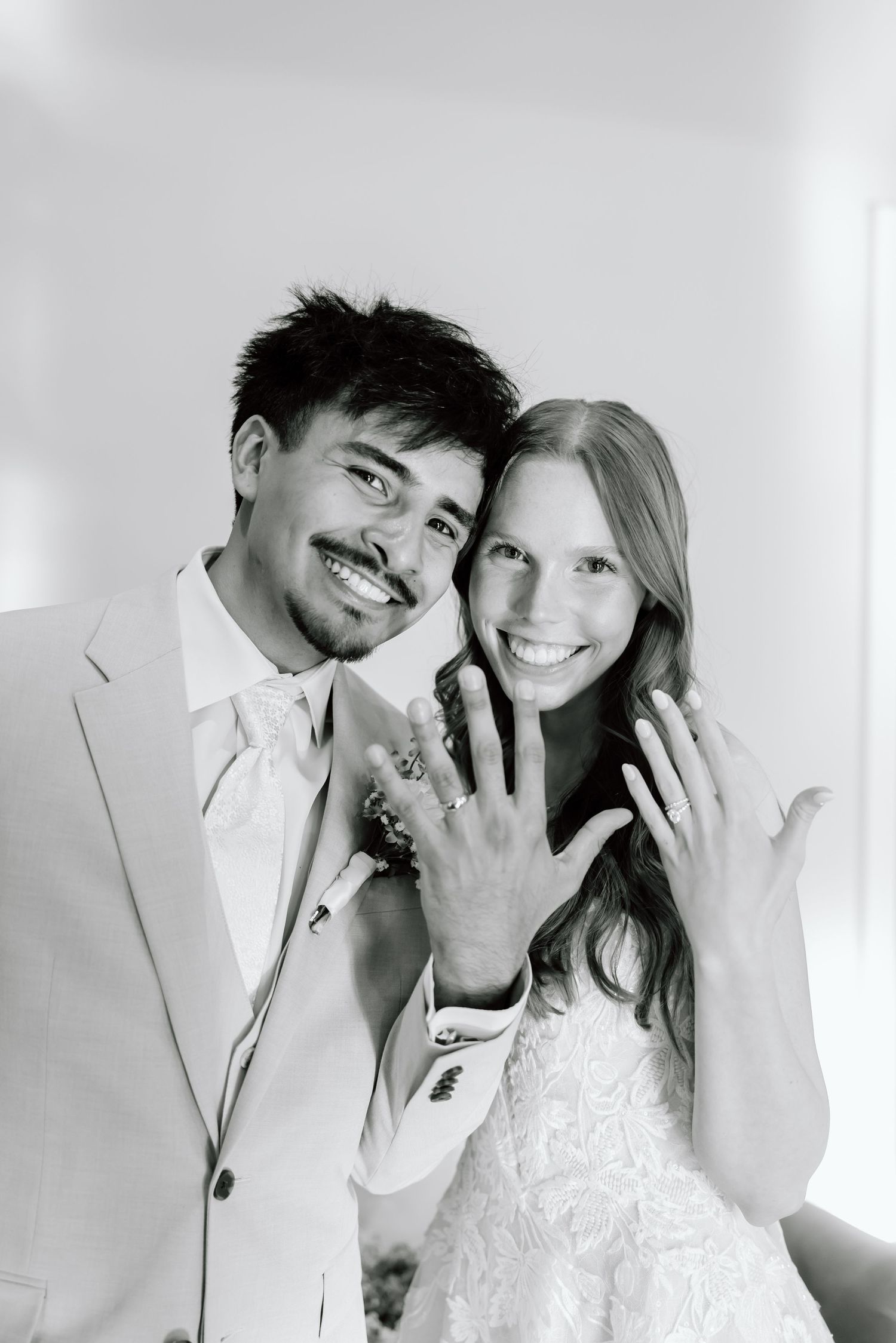 Newlywed couple smiling and showing off their wedding rings in a black and white portrait photo.