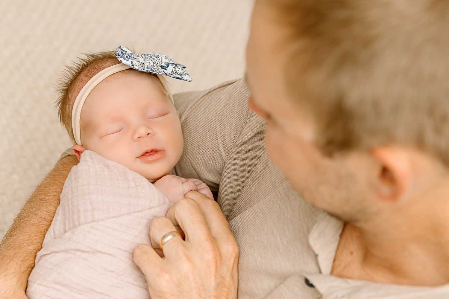 Tender moment of adult holding sleeping newborn with silver bow headband.