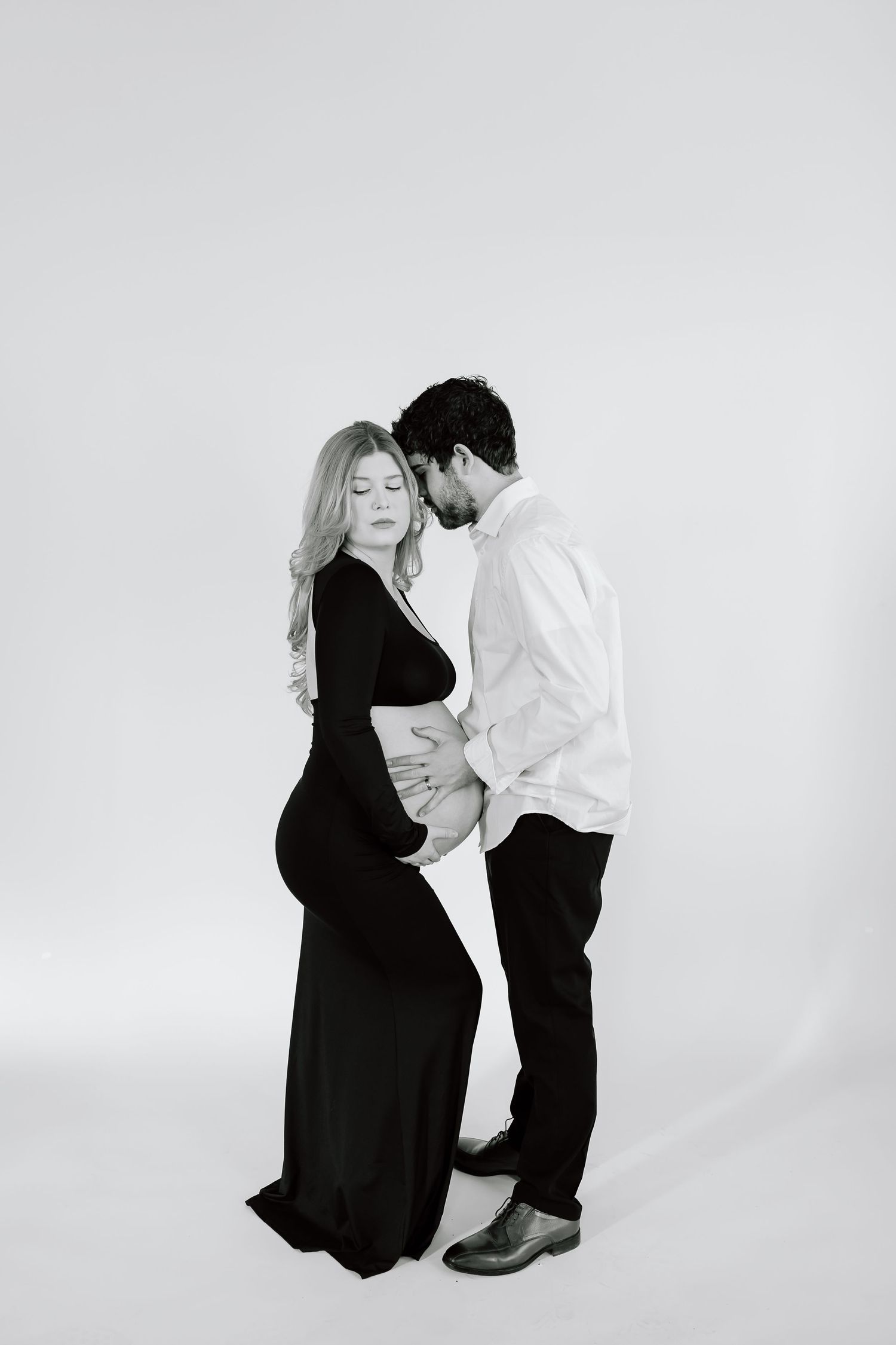 Elegant maternity photoshoot in black and white featuring a couple posing intimately against a light background.