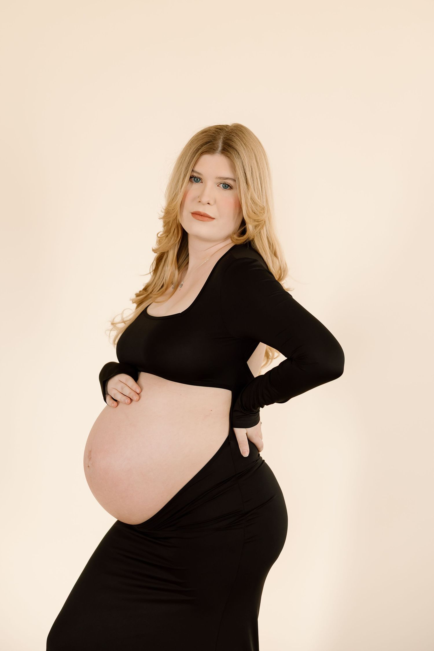 Side view maternity portrait of a woman in black dress highlighting her pregnancy.