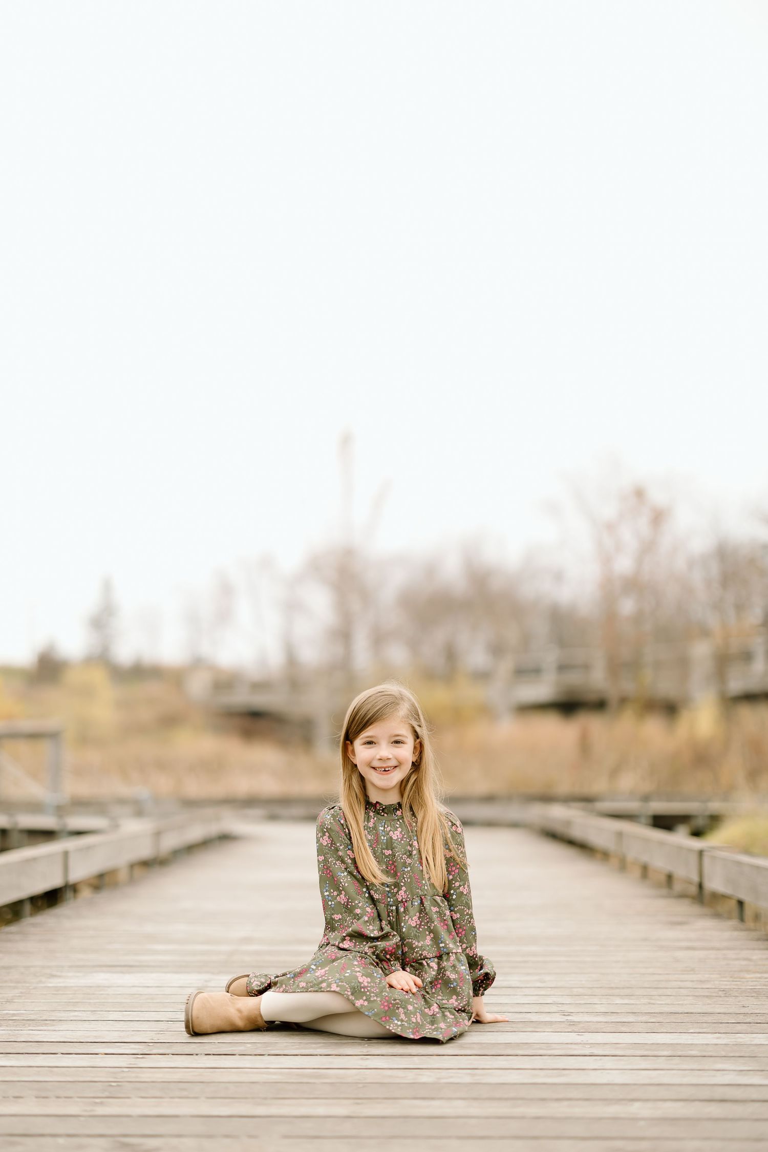 A child sits gracefully on a wooden boardwalk for a portrait session.