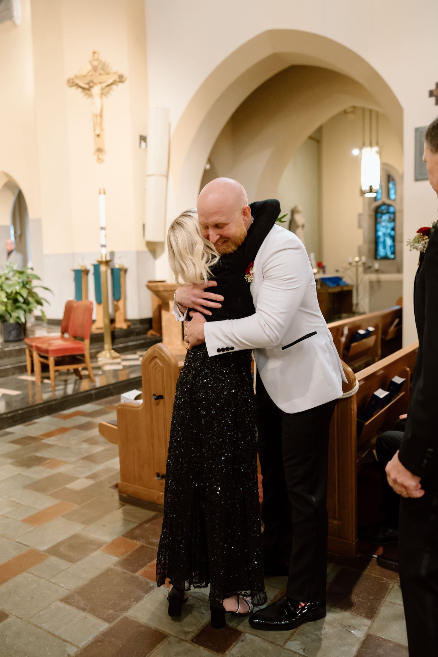 Two people share an emotional embrace inside a church with wooden pews and arched architecture visible in the background.