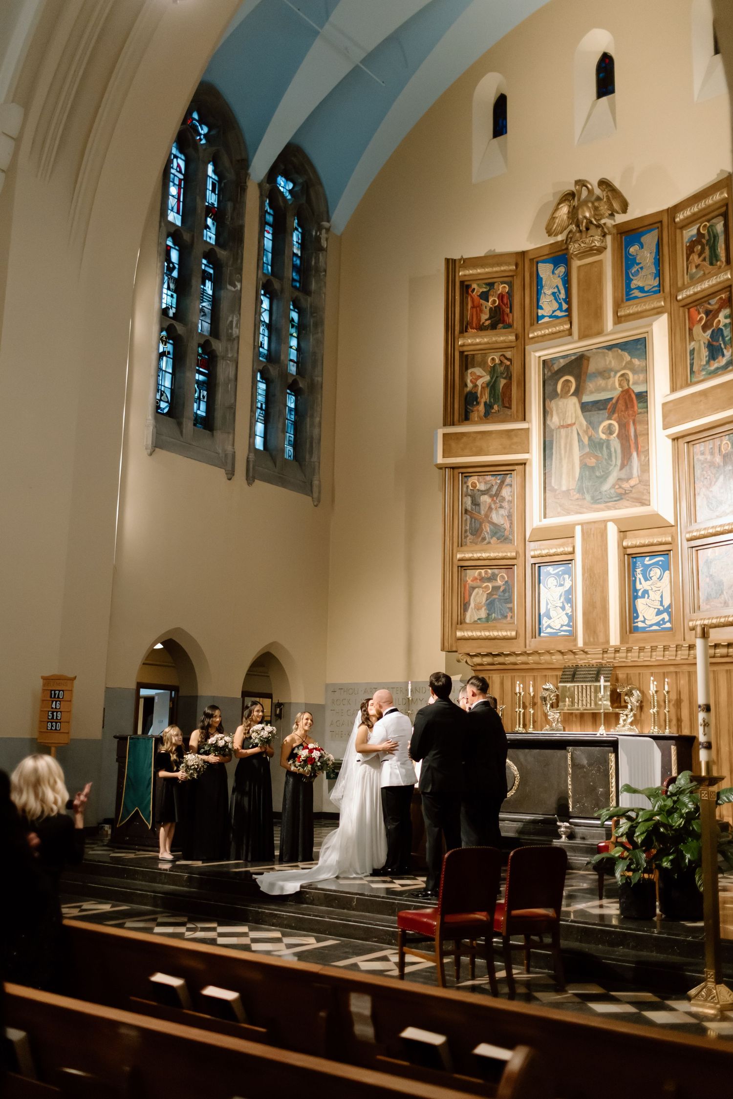 Wedding ceremony in progress inside a traditional church with stained glass windows and religious artwork on display.
