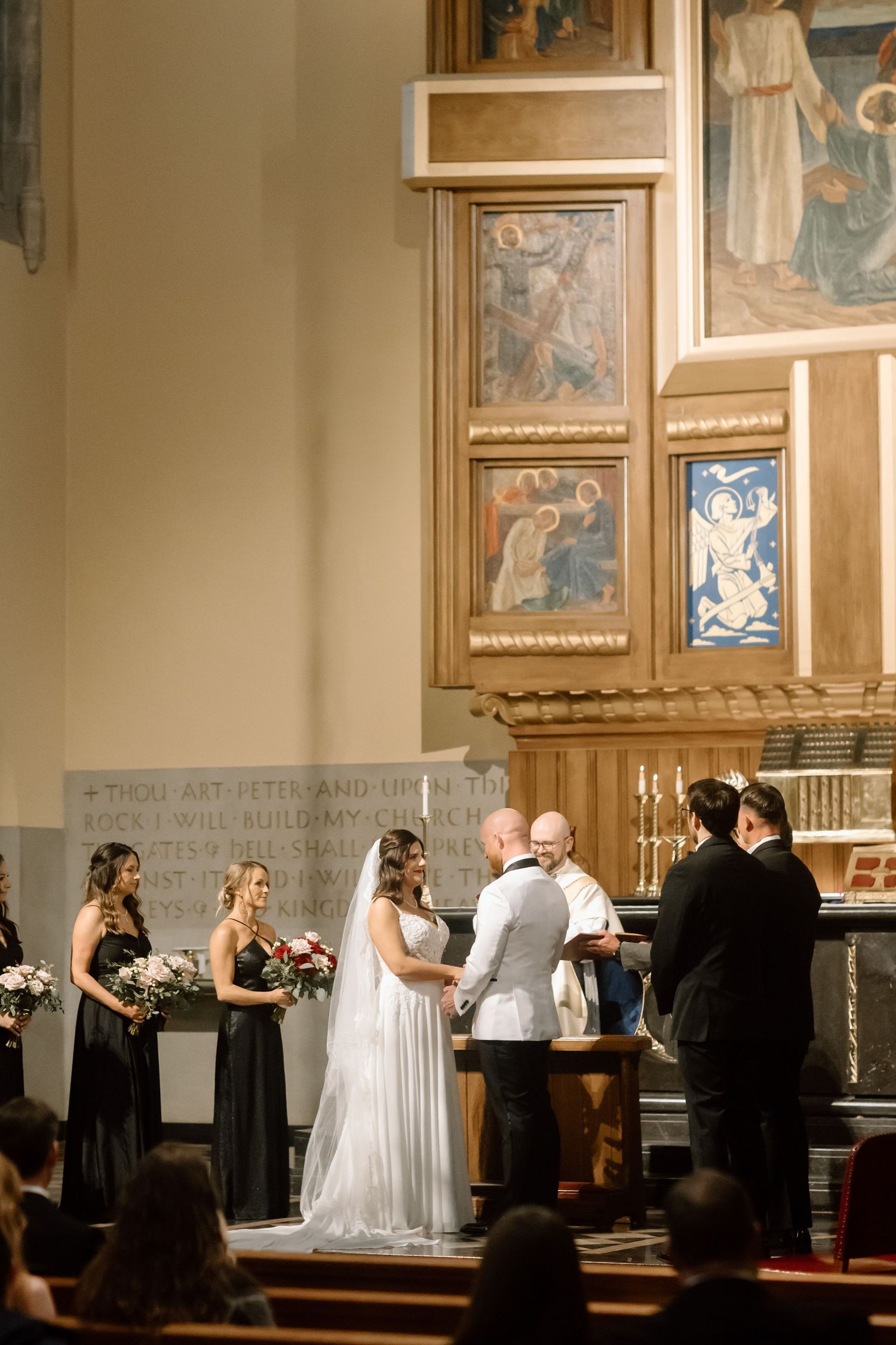 Wedding ceremony taking place in an ornate church with couples lined up along the altar during a group ceremony.