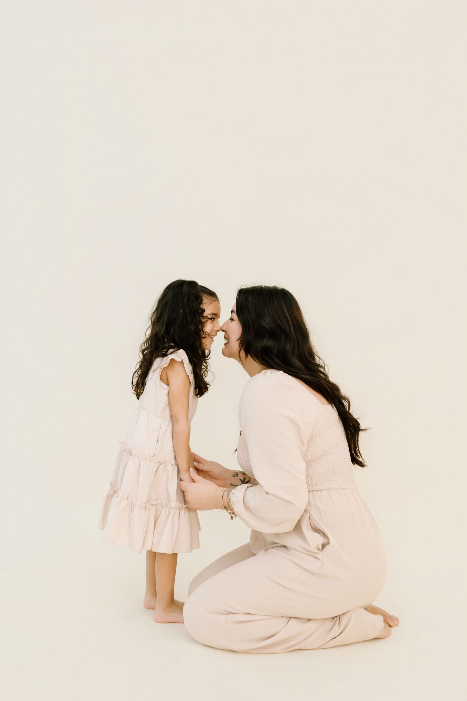 A touching moment between parent and child wearing matching light pink dresses against a white background.