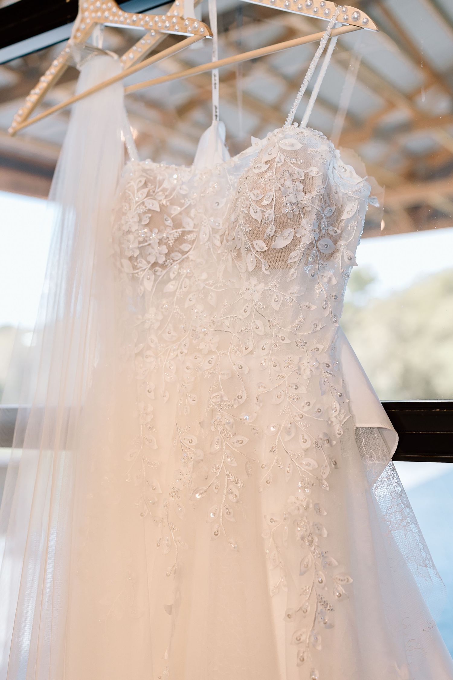 Close-up view of delicate white lace and beading details on a wedding dress hanging from a hanger.