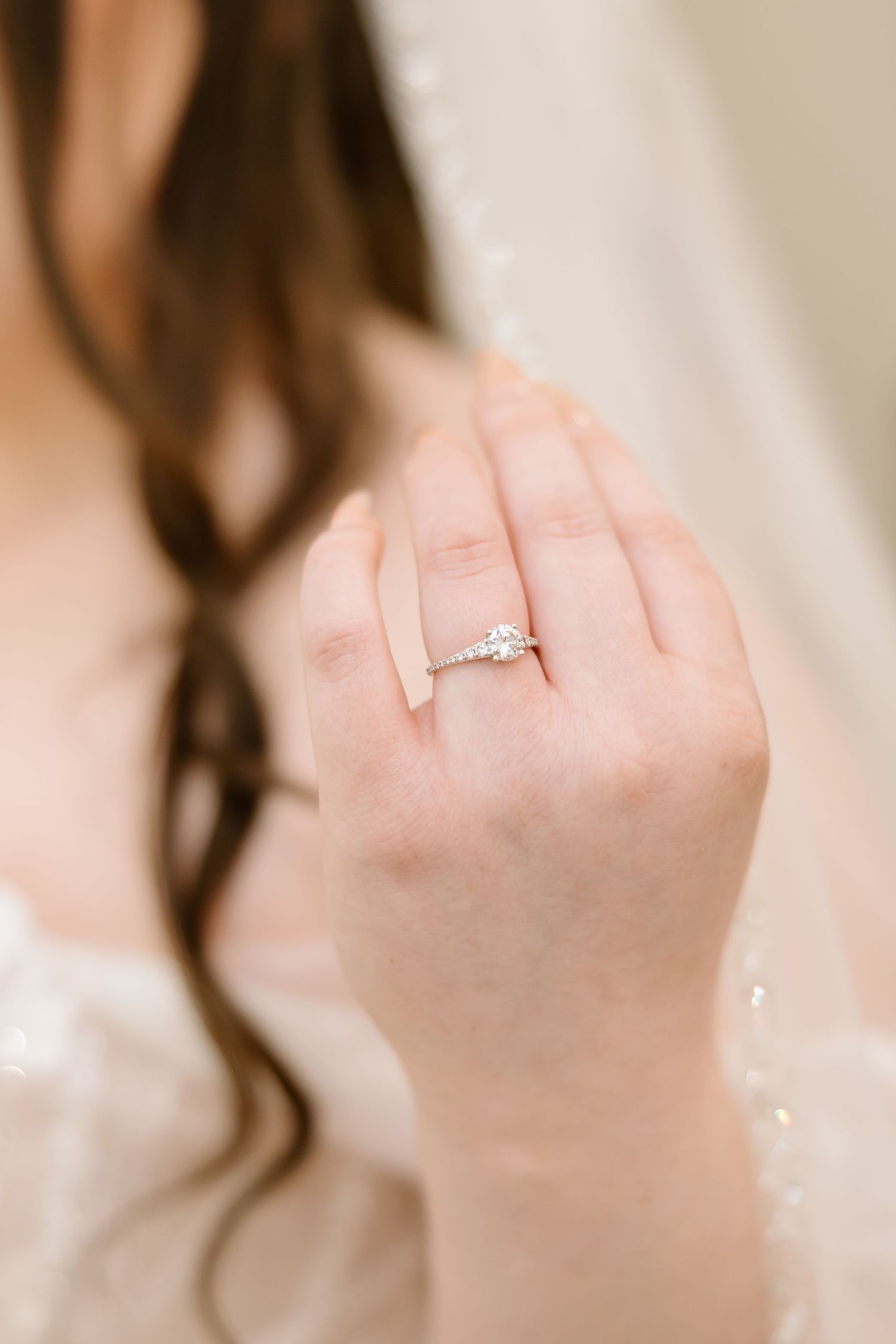 Close-up view of a sparkling diamond engagement ring on a delicate hand with neutral manicured nails.