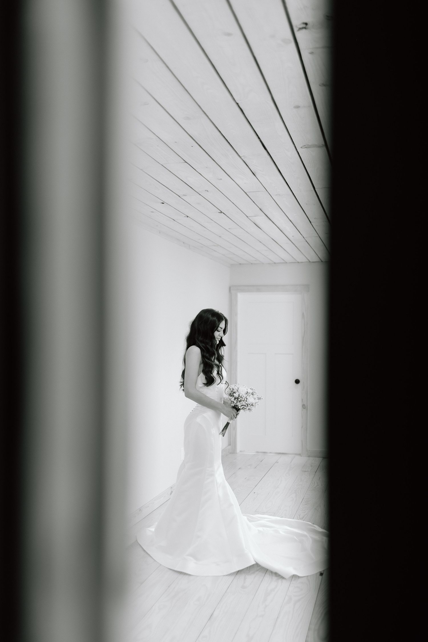 A bride in a white wedding dress poses in a minimalist white hallway creating a striking black and white composition.