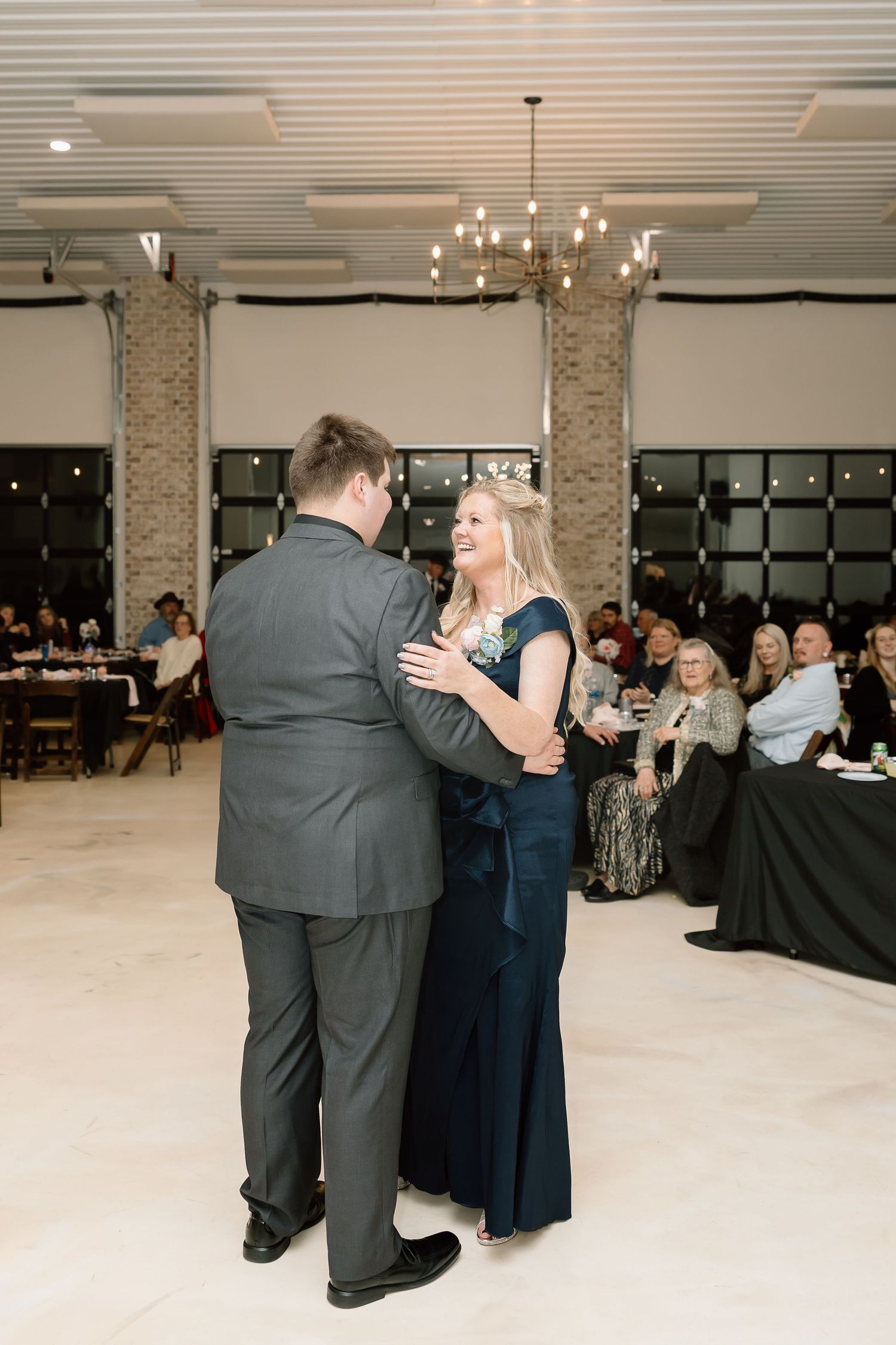 Wedding guests dancing together in formal attire at an elegant indoor reception venue with modern lighting.