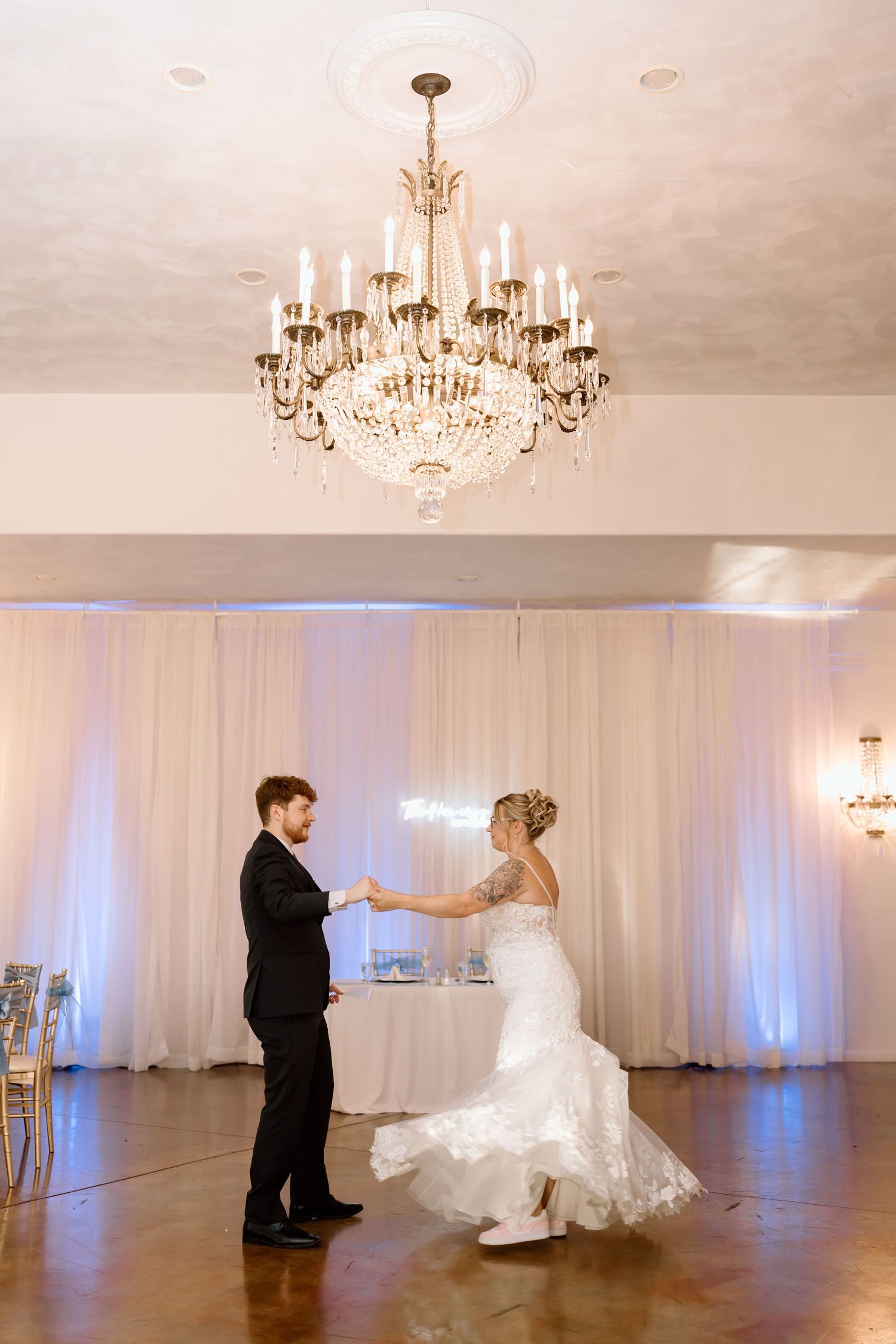 Elegant wedding dance sequence in white ballroom with crystal chandeliers and blue uplighting along white draped walls.