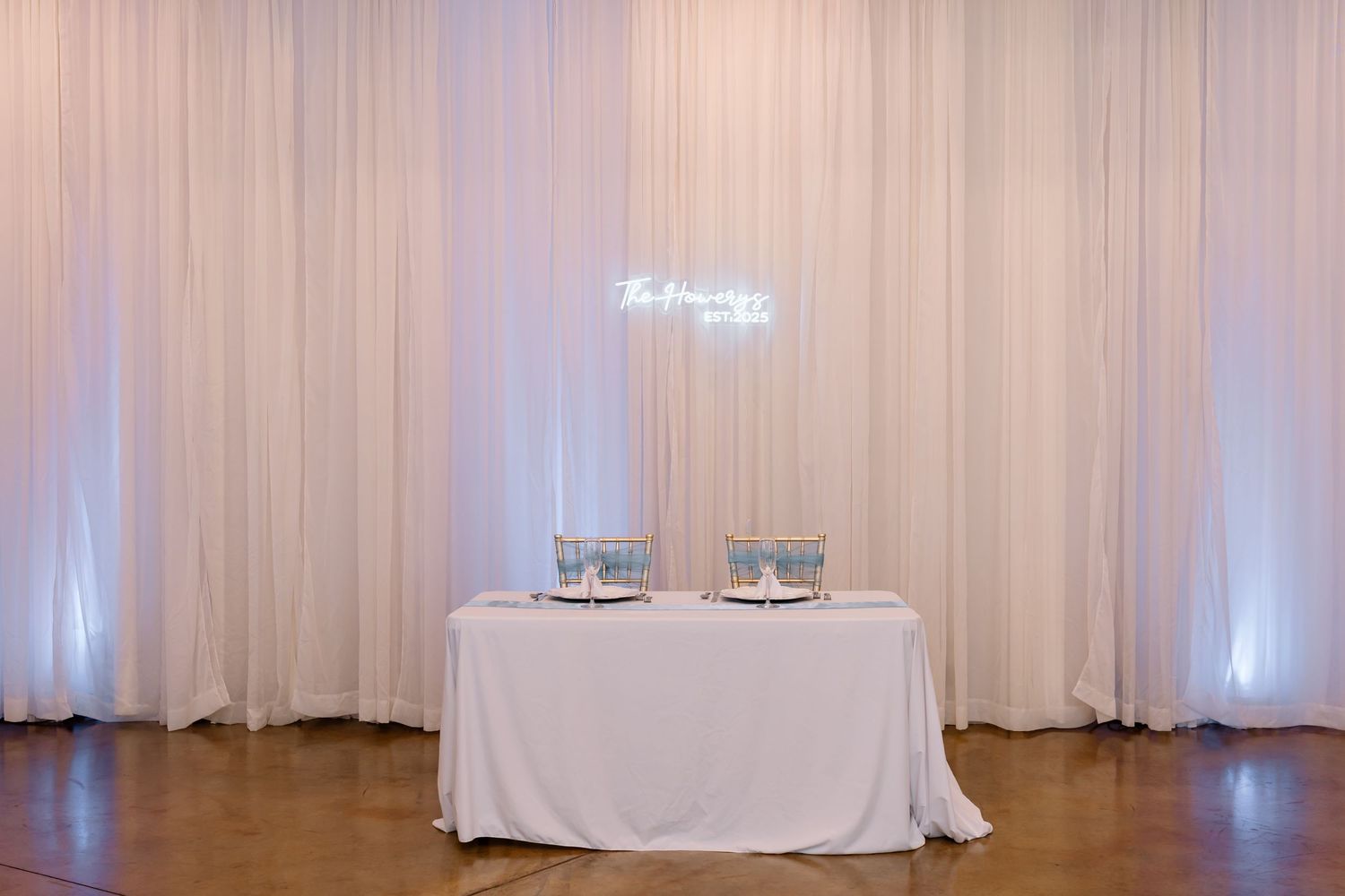 White fabric drapes elegantly line a wall in a reception or event space with soft lighting and a small table visible.