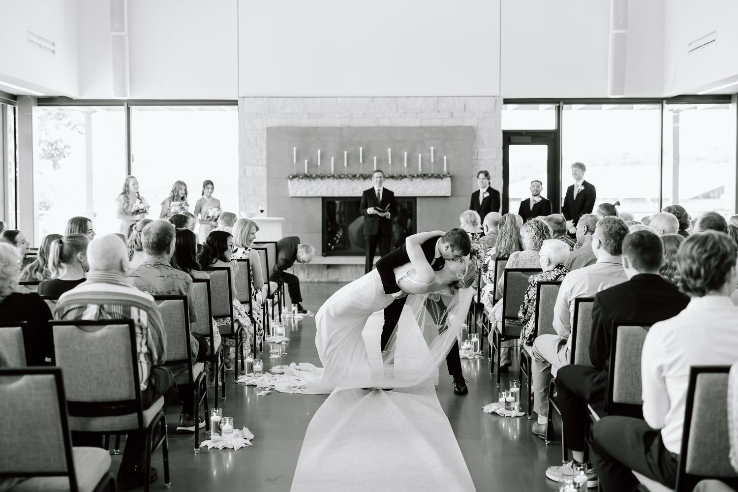 People seated in a bright minimalist banquet hall during an event, with floor-to-ceiling windows and white decor.