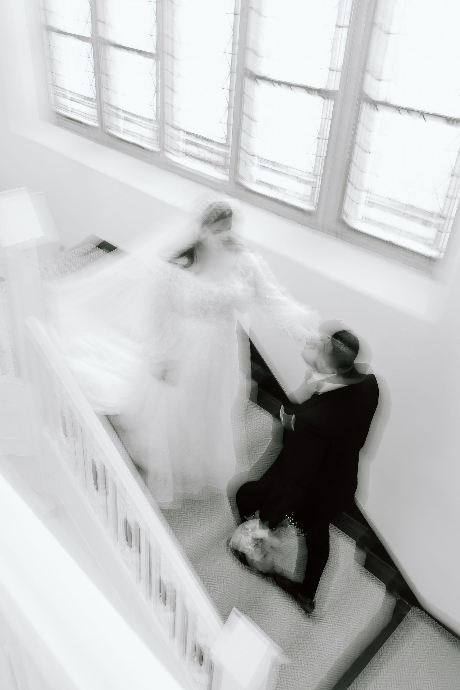 Black and white motion blur photo of bride and groom descending elegant staircase on wedding day.
