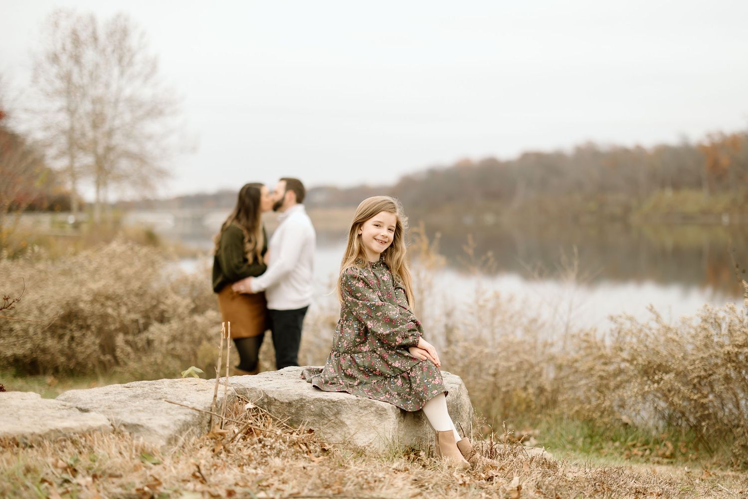 Person in floral dress sitting on rock with couple embracing in background.